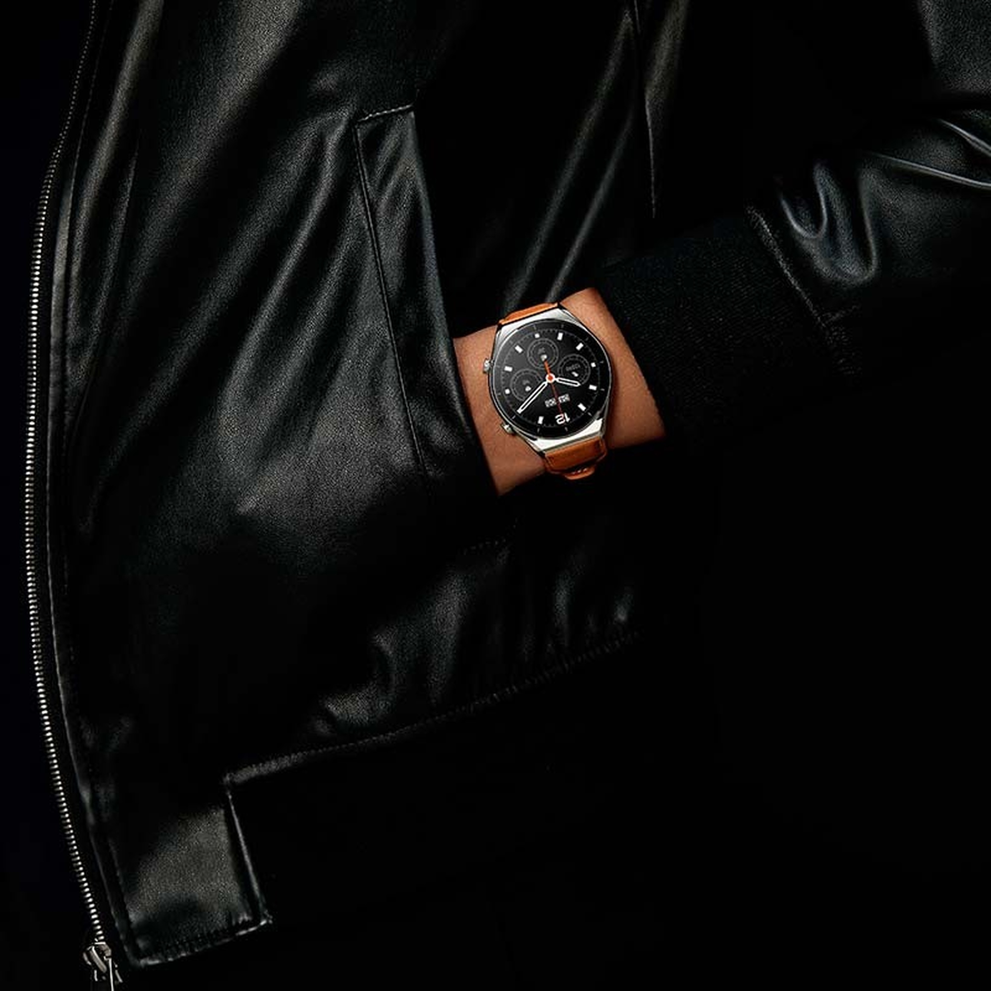 Osoba nosząca czarną skórzaną kurtkę i zegarek z brązowym paskiem. Zegarek ma czarną tarczę.