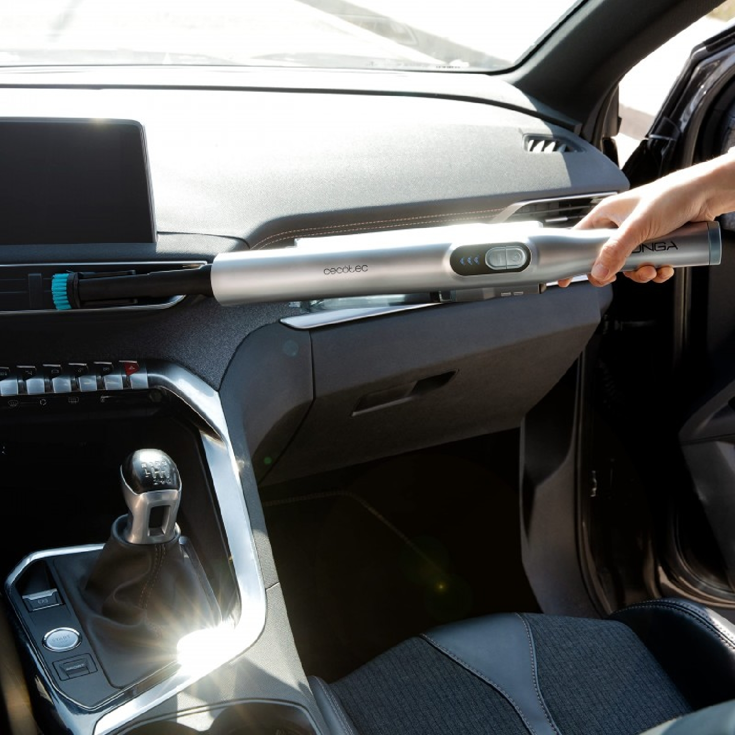 Persona che tiene un aspirapolvere per auto argentato all'interno di un'auto, vicino al cruscotto.