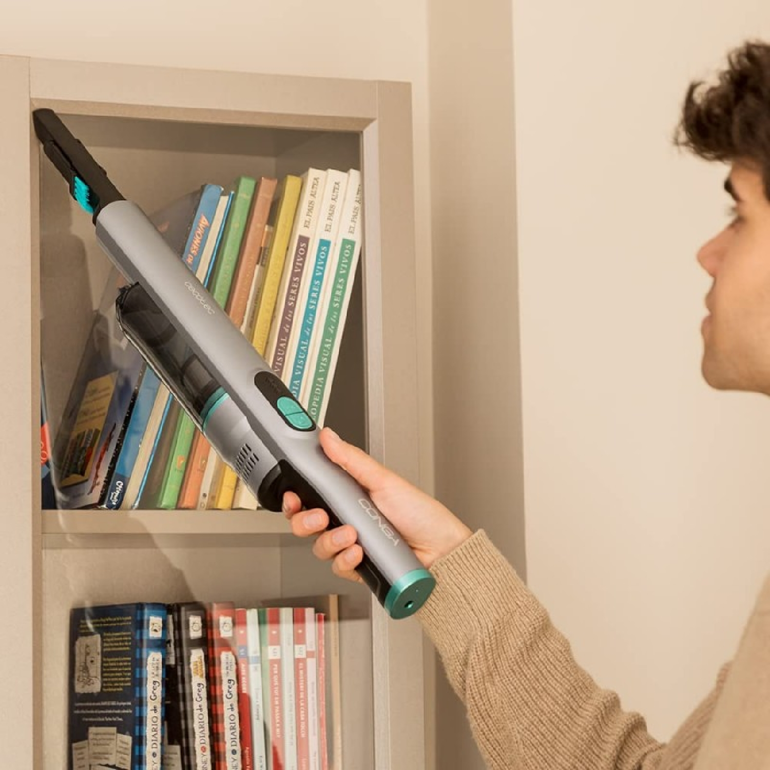 Uomo che pulisce la libreria con un aspirapolvere portatile.