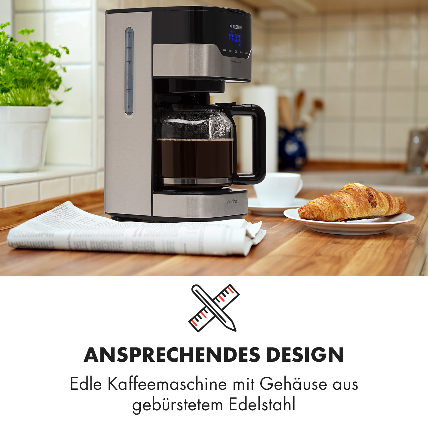 Cafetera con periódico, cruasán y planta, mesa de madera.