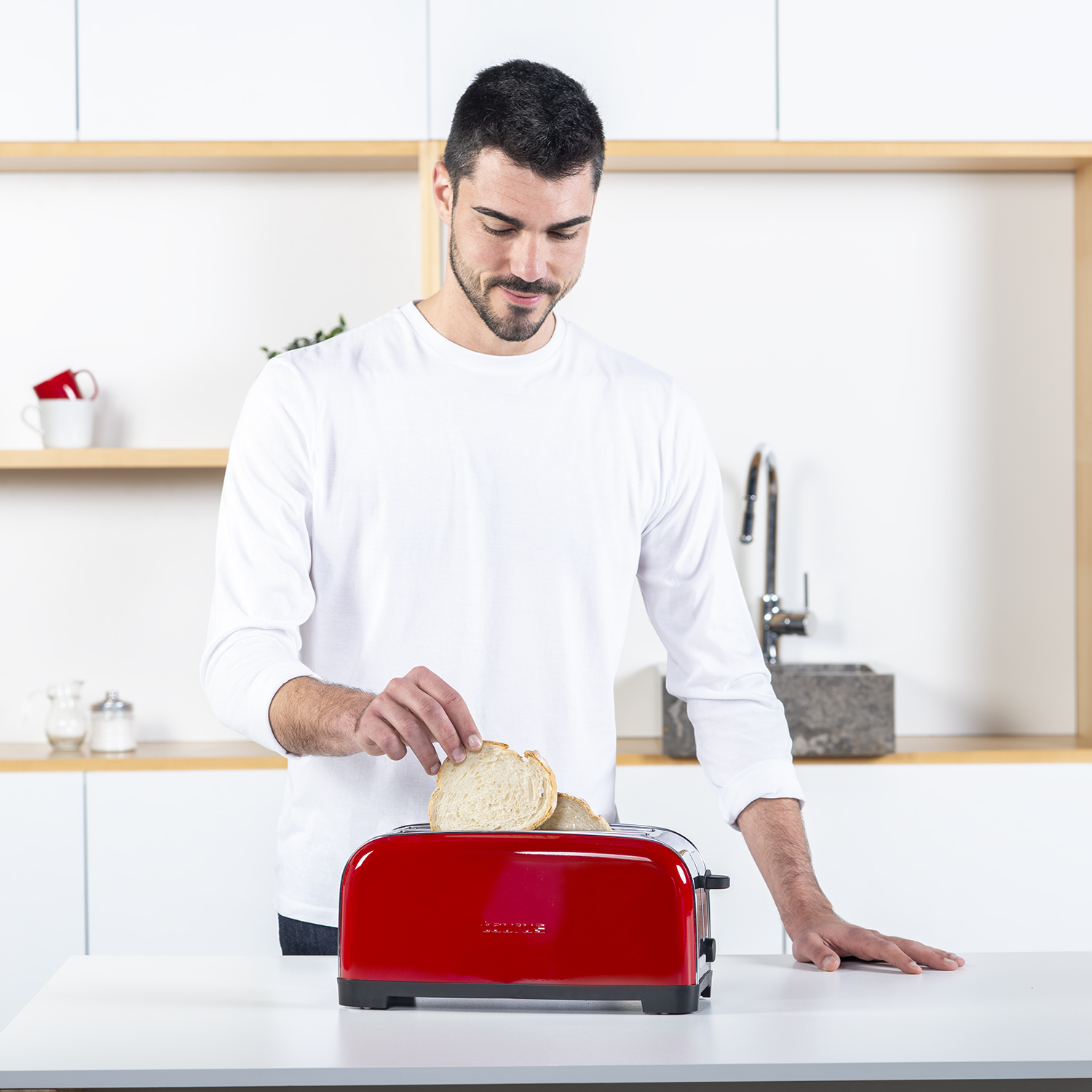 Hombre tostando pan con tostadora roja. Entorno de cocina.