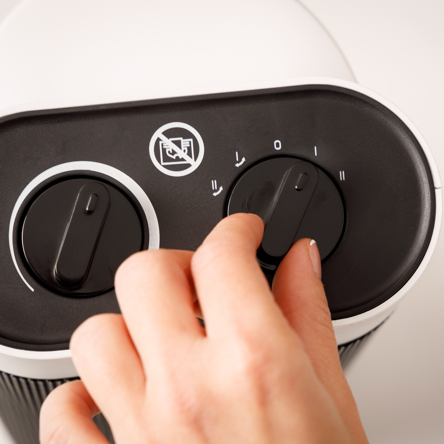 Una mano gira un dial en un electrodoméstico blanco y negro, ajustando la velocidad.