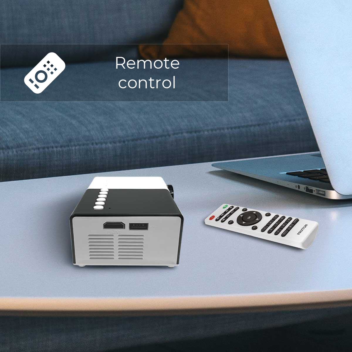 A black and white projector with a remote control on a table. A laptop is visible in the background.