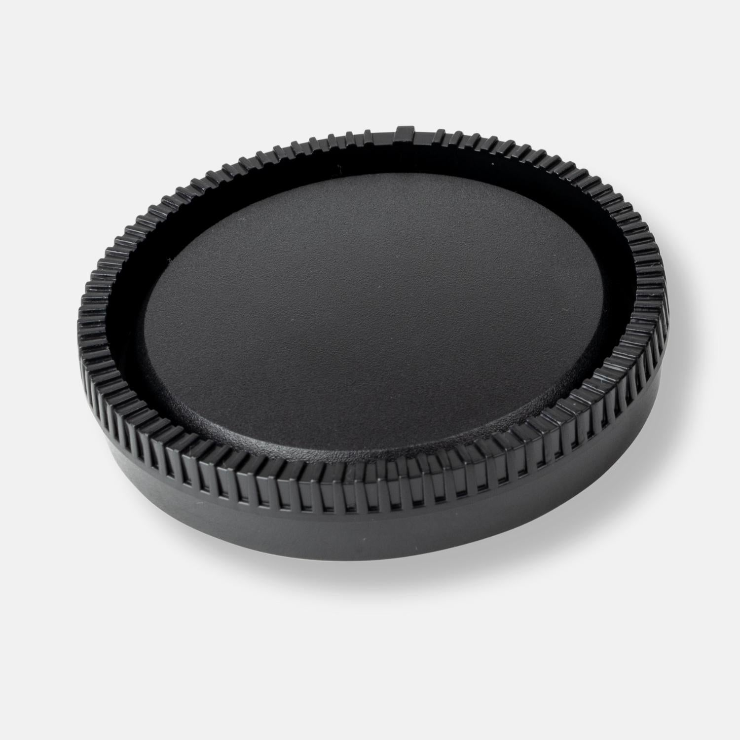 Eine schwarze Objektivkappe mit geriffeltem Rand, isoliert auf weißem Hintergrund.