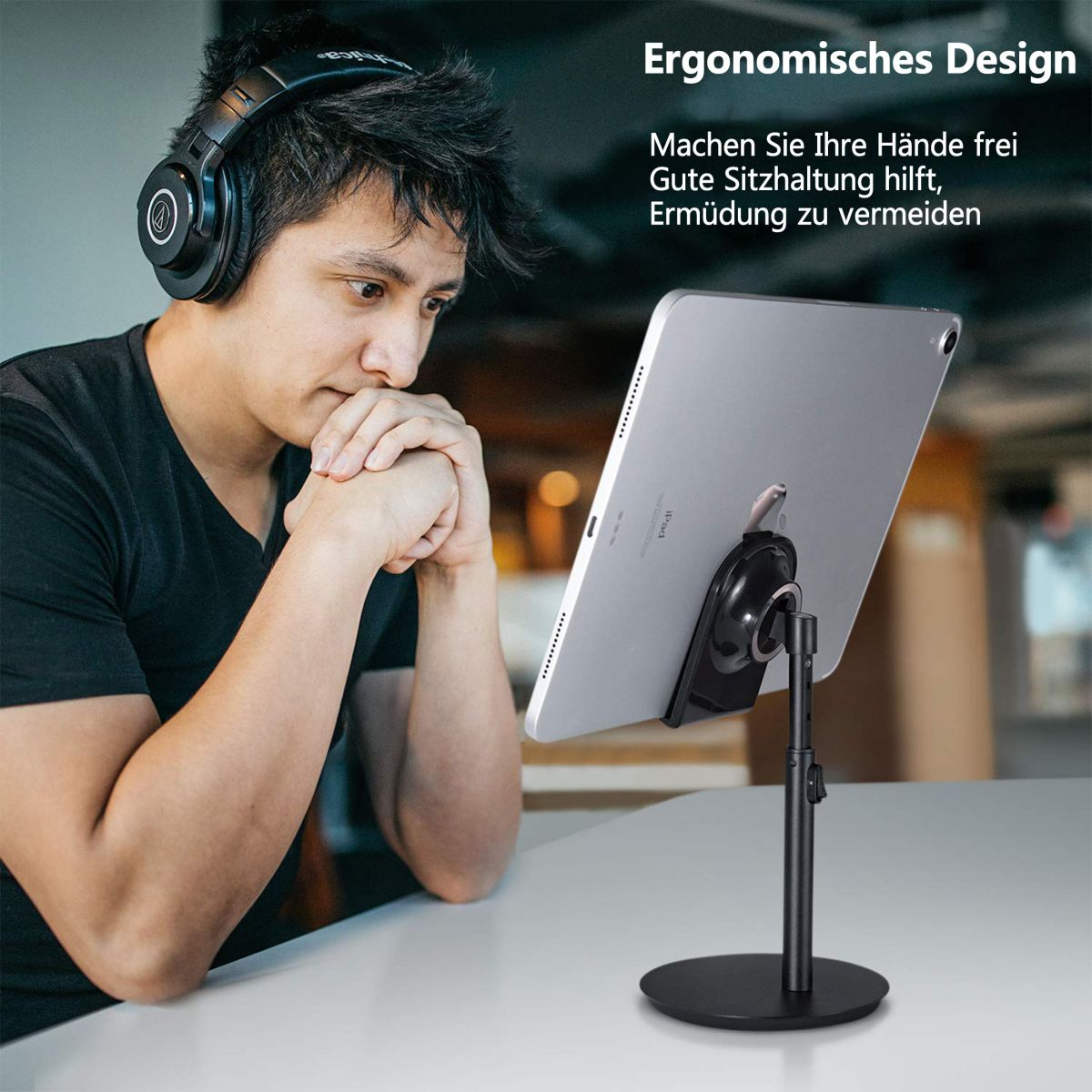 Mann mit Kopfhörern schaut auf Tablet auf Ständer. Das Tablet ist silberfarben.