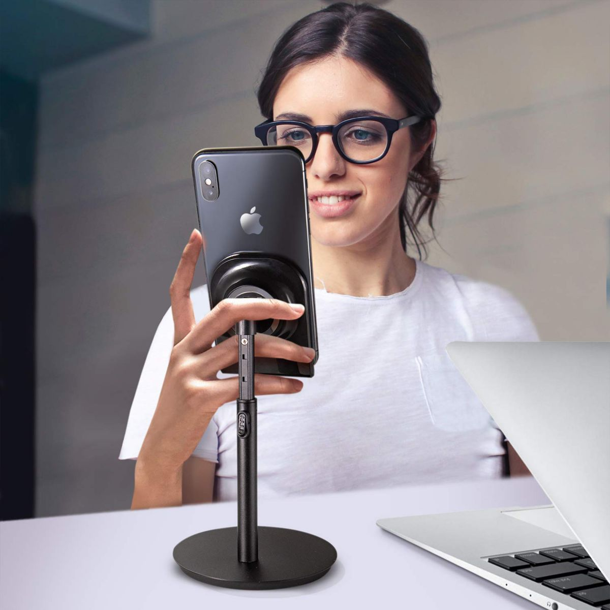 Frau mit Brille benutzt Telefon auf Ständer, Laptop auf dem Schreibtisch.