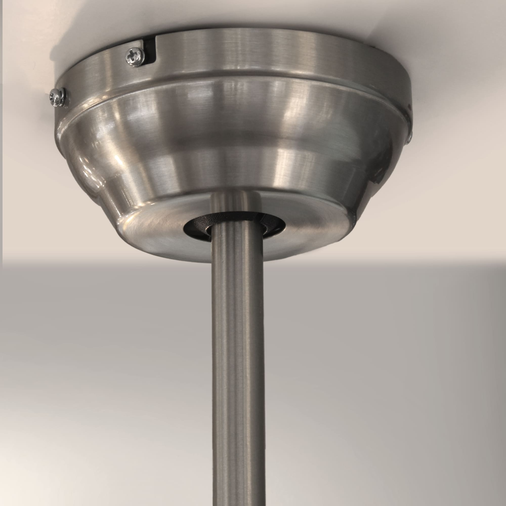 Primer plano del motor de un ventilador de techo plateado con varilla de conexión, fondo blanco.