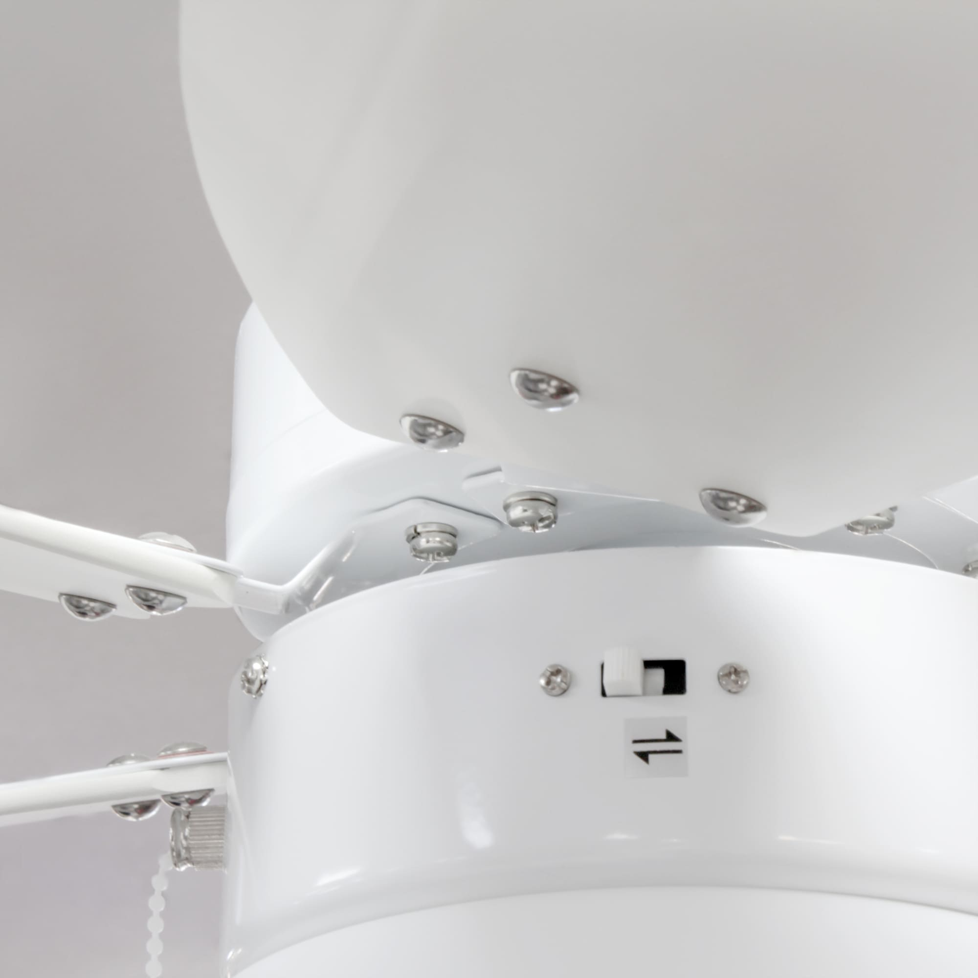 Primer plano de la carcasa del motor, el interruptor y los detalles de montaje de un ventilador de techo blanco.