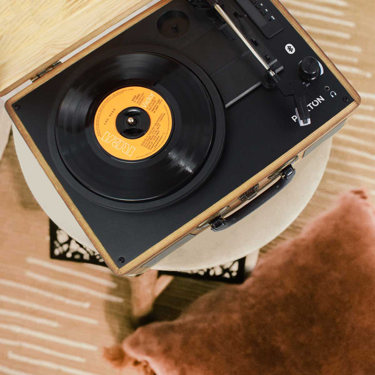 Odtwarzacz płyt z płytą na wierzchu. Jest na małym stoliku z różową poduszką. Widok z góry.