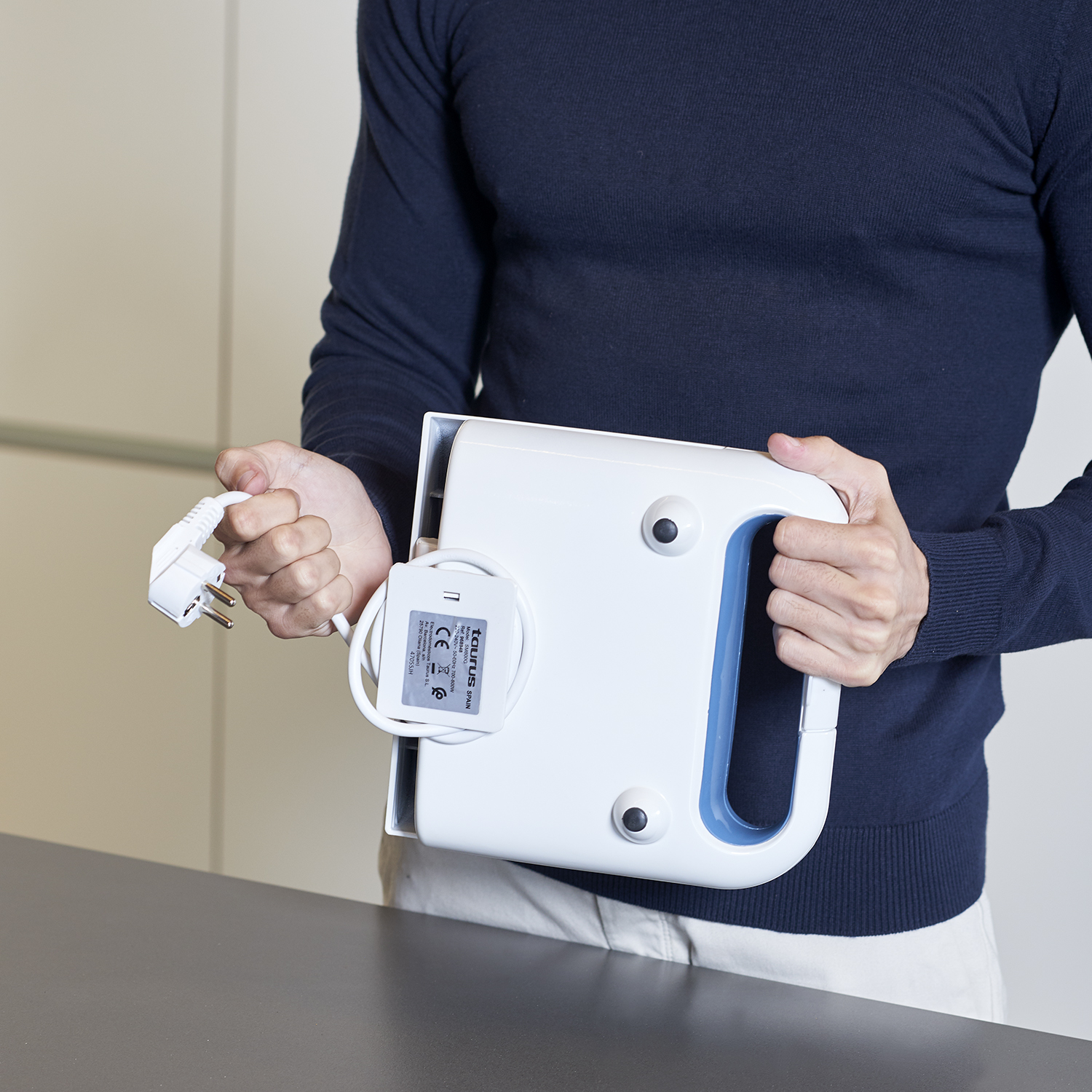 Una persona sostiene un electrodoméstico de cocina blanco y azul con enchufe y cable.