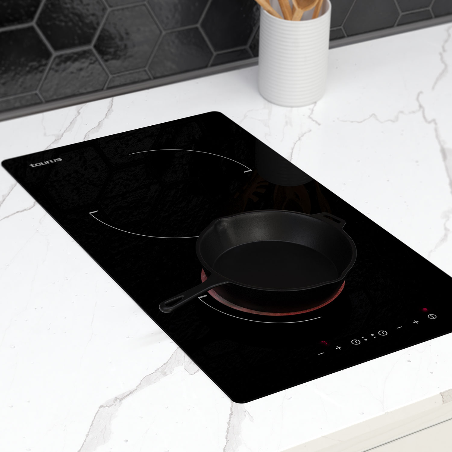 Una placa de inducción con una sartén negra encima. Encimera blanca y azulejos hexagonales negros.