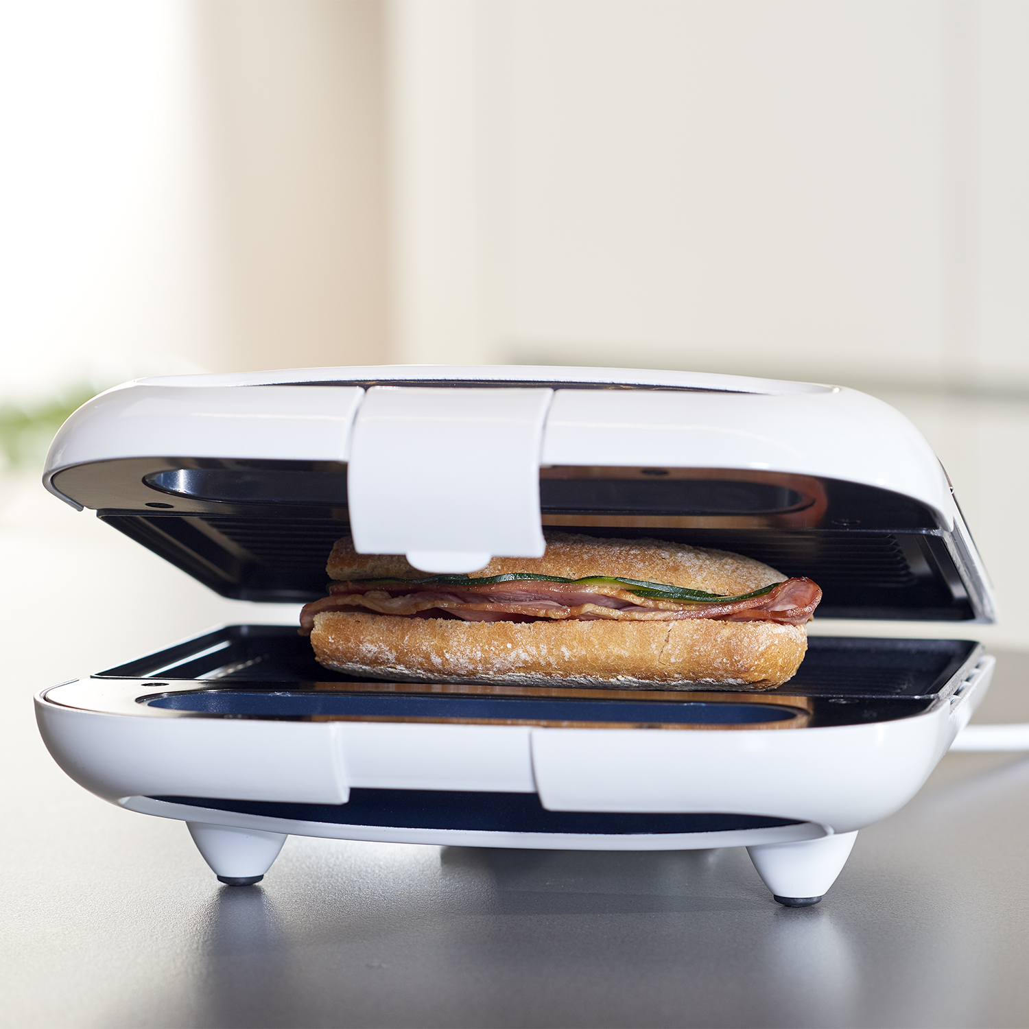 Sandwich maker aperto con sandwich con pancetta ed erbe verdi.