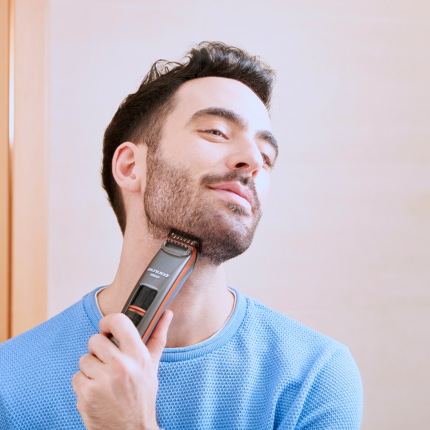 Un hombre se afeita la barba con una recortadora negra y naranja, mirándose en un espejo.