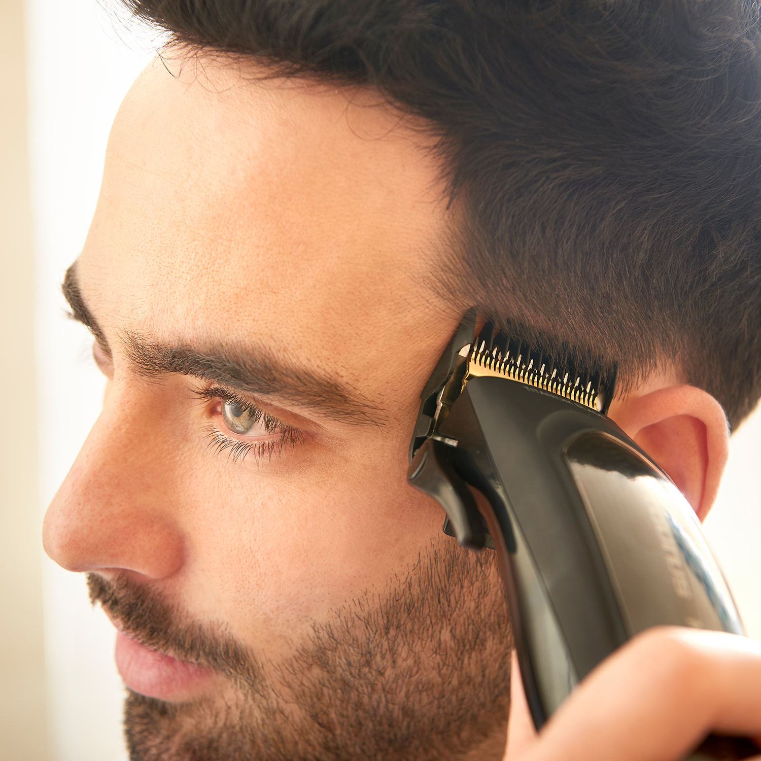 Un uomo si taglia i capelli con un tagliacapelli nero. Il tagliacapelli è tenuto vicino alla sua testa.