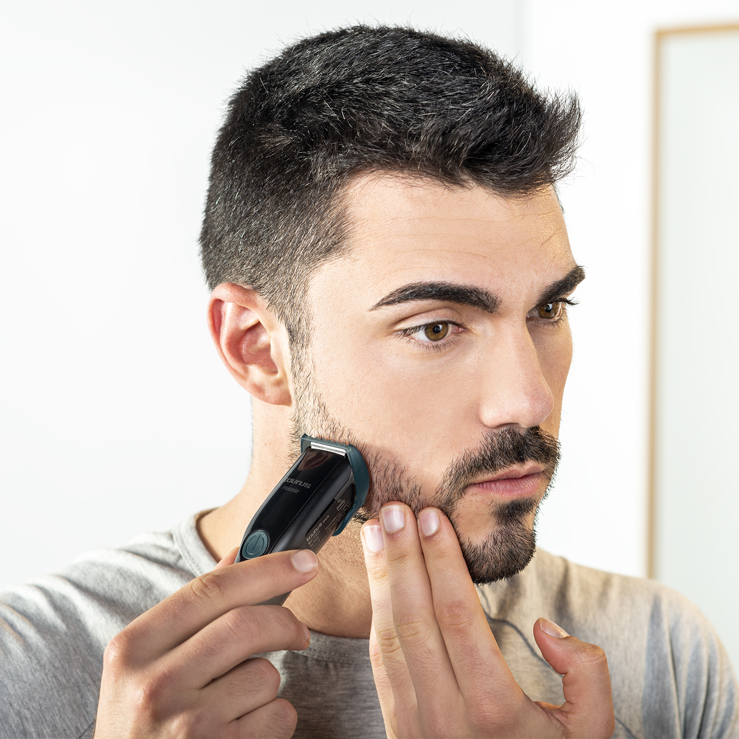 Hombre usando un recortador de barba, mirándose al espejo.