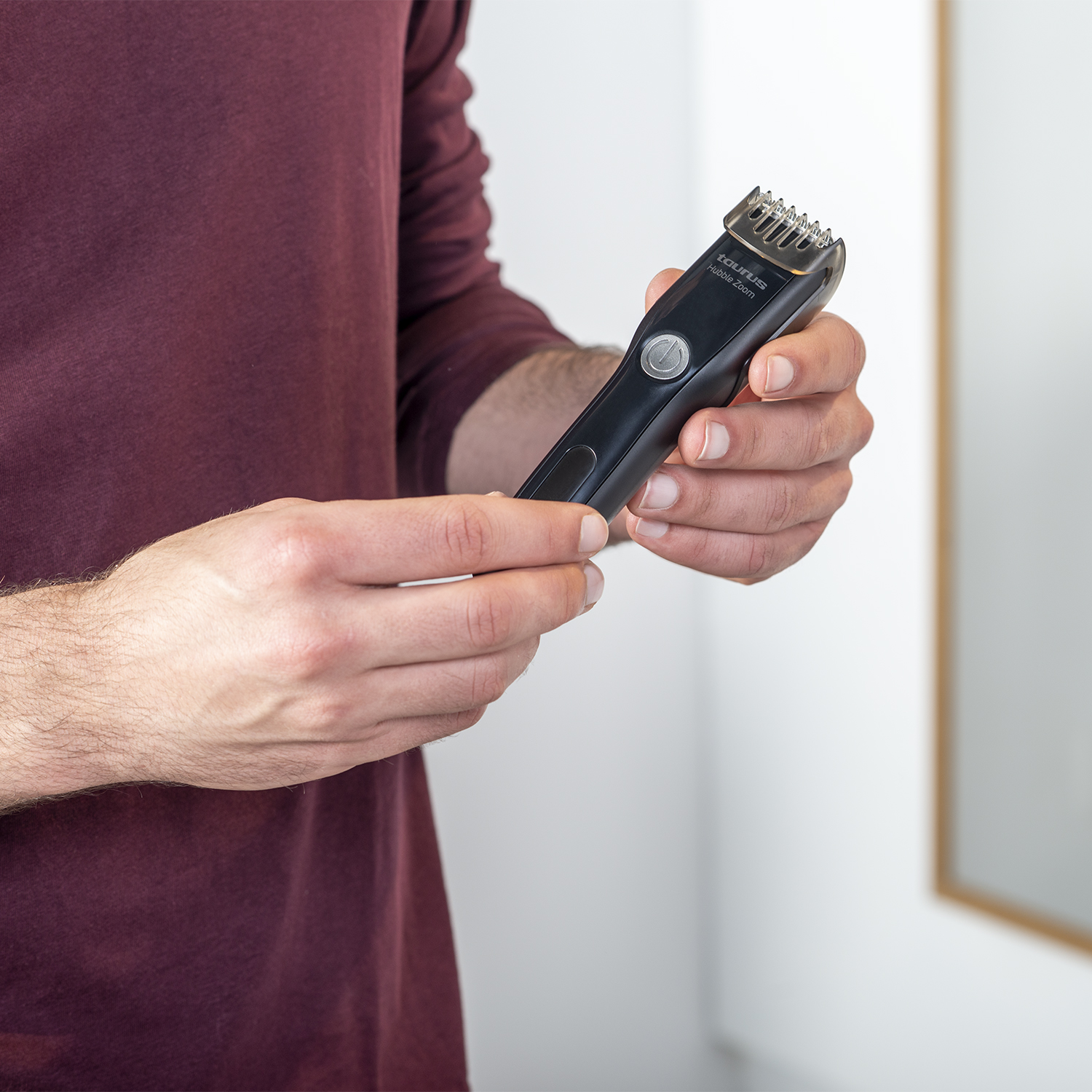 Un hombre sosteniendo una recortadora de barba negra, mostrando el dispositivo y su botón de encendido.