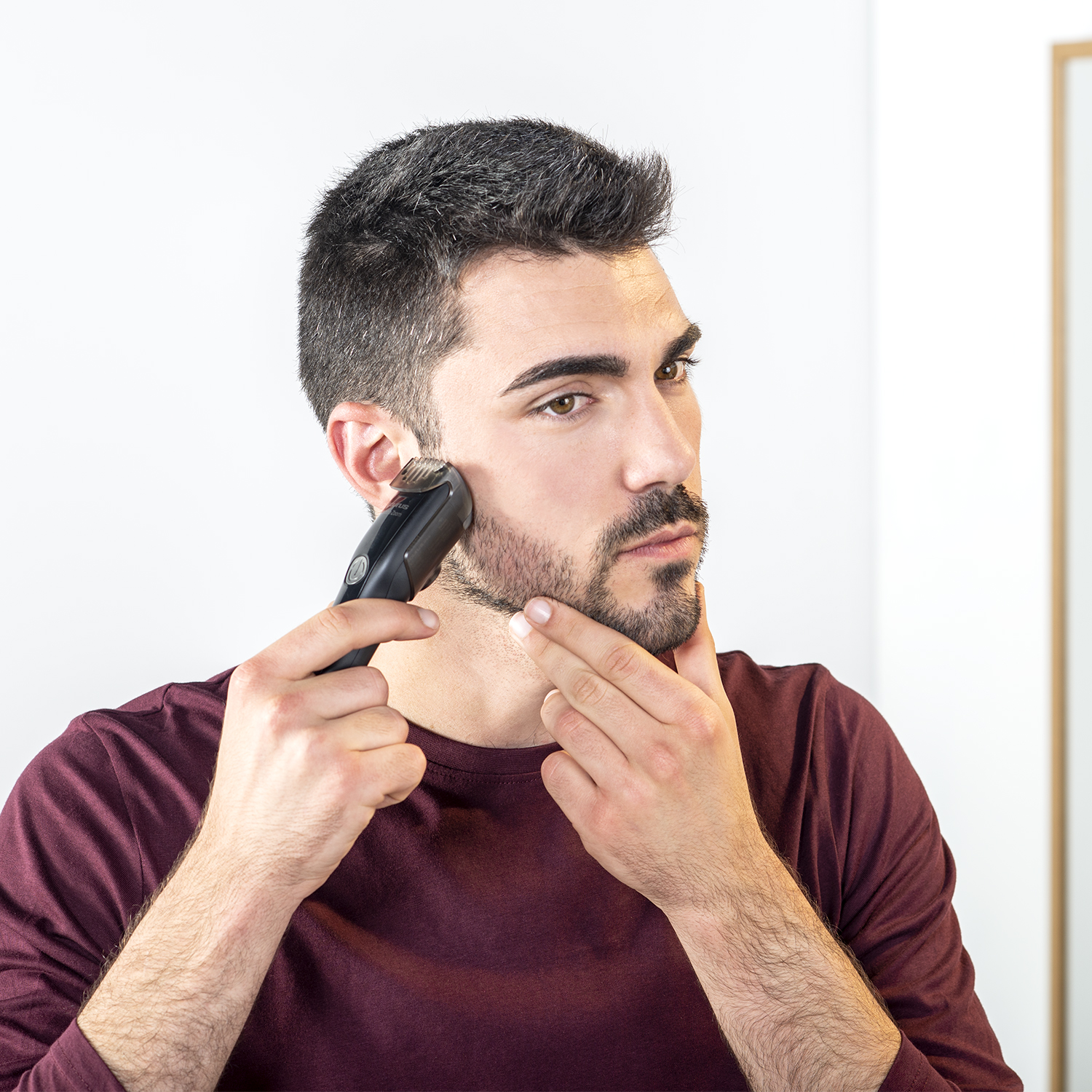 Uomo che si taglia la barba con un trimmer elettrico nero davanti allo specchio.