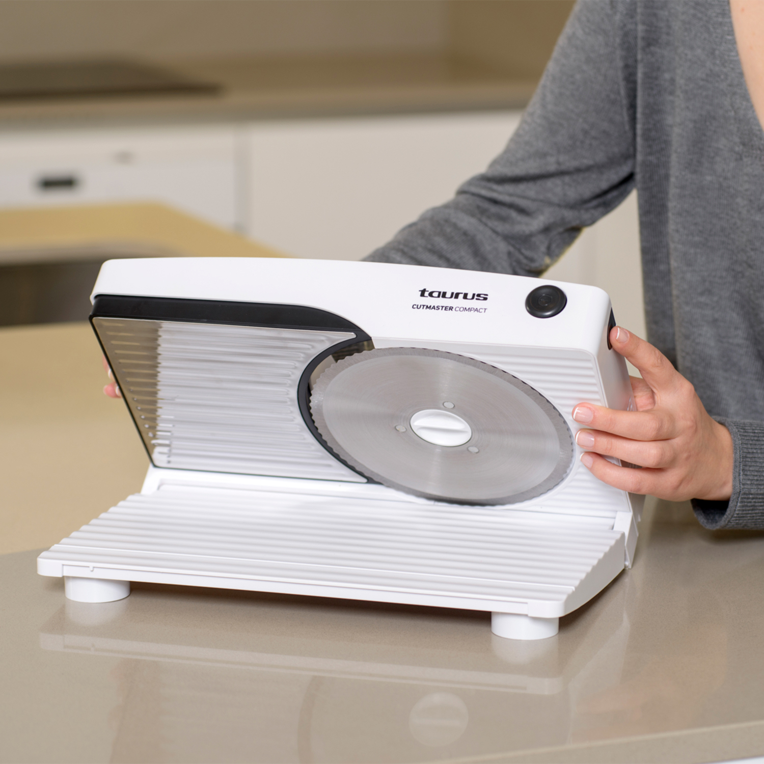 Una mujer usando una cortadora de alimentos blanca Taurus Cutmaster Compact. La cuchilla es visible.