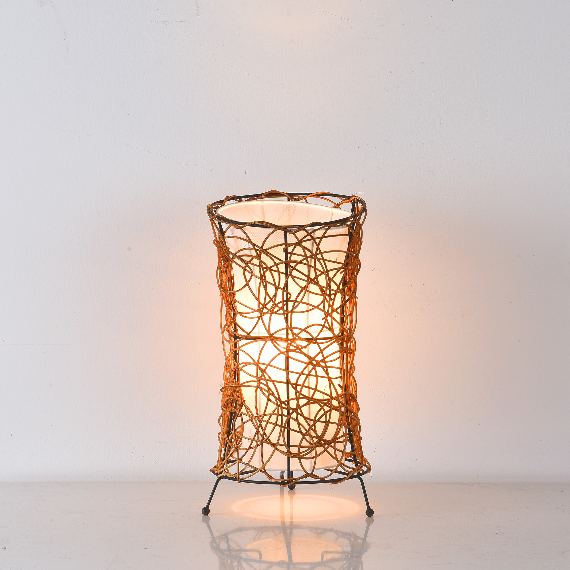 Eine hohe, zylindrische Lampe aus geflochtenem braunen Material, von innen beleuchtet.