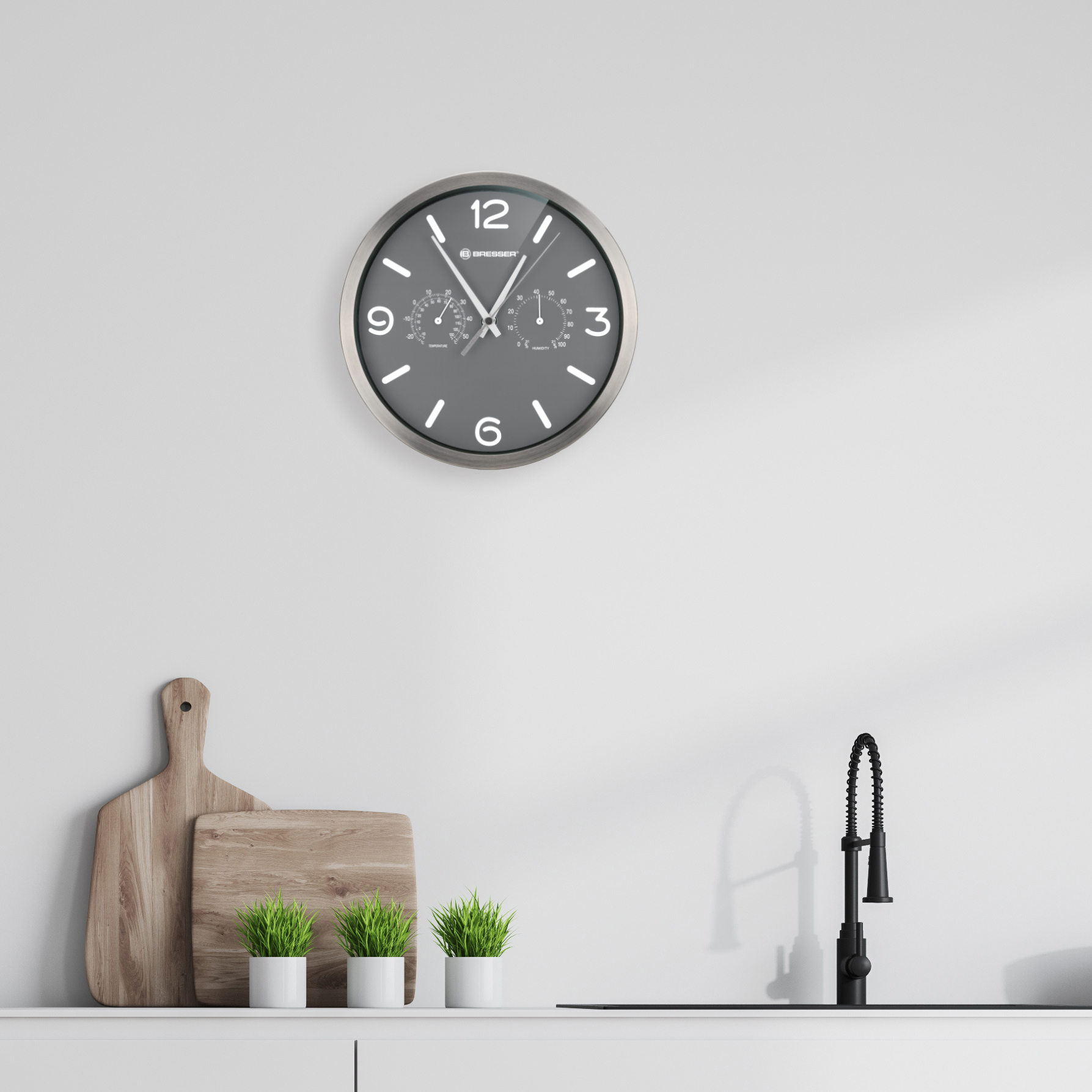 Eine graue Uhr an einer weißen Wand über einem Waschbecken.