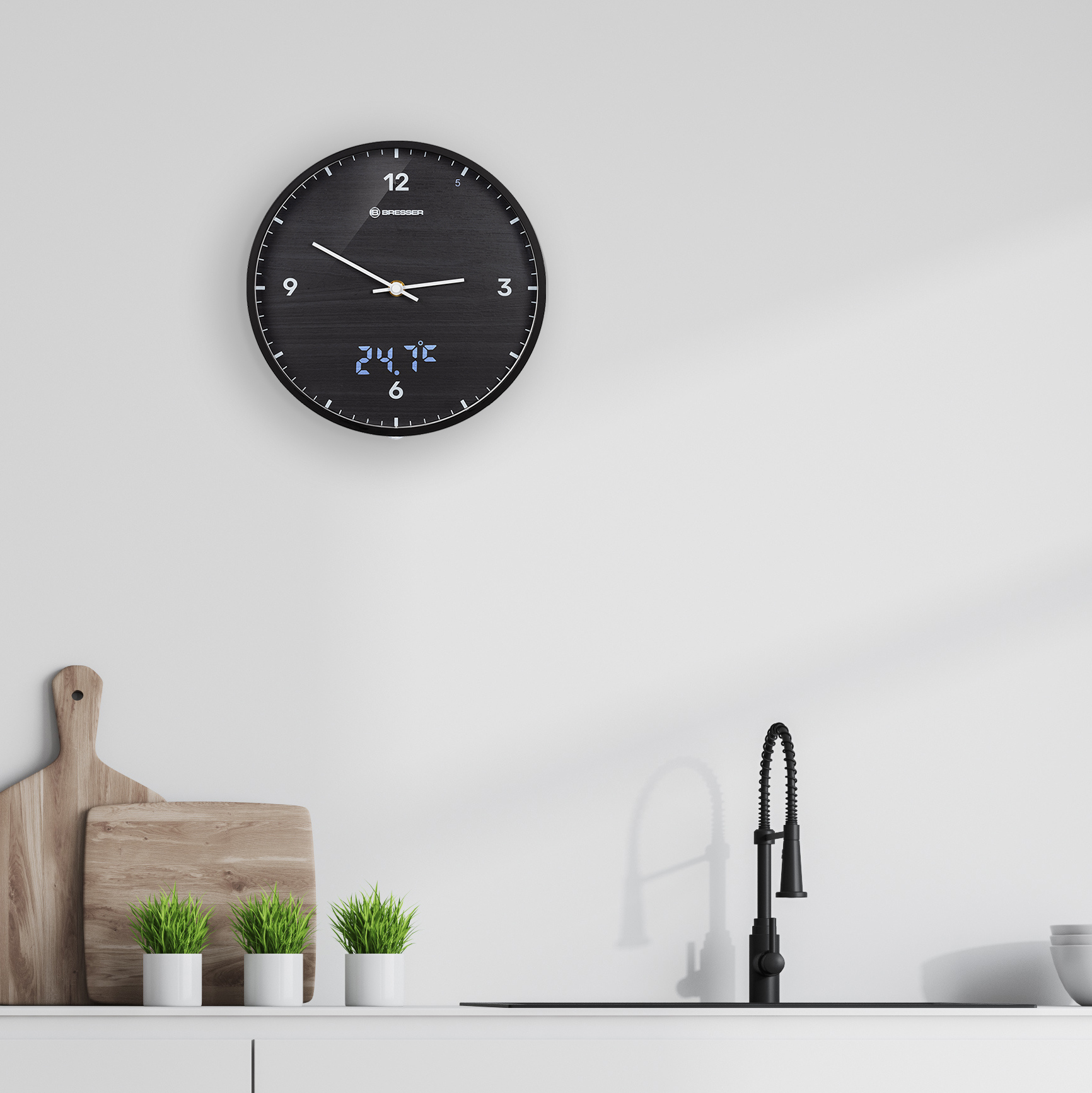 Un reloj de pared negro con pantalla digital, que muestra la hora y la temperatura, sobre un fregadero de cocina.