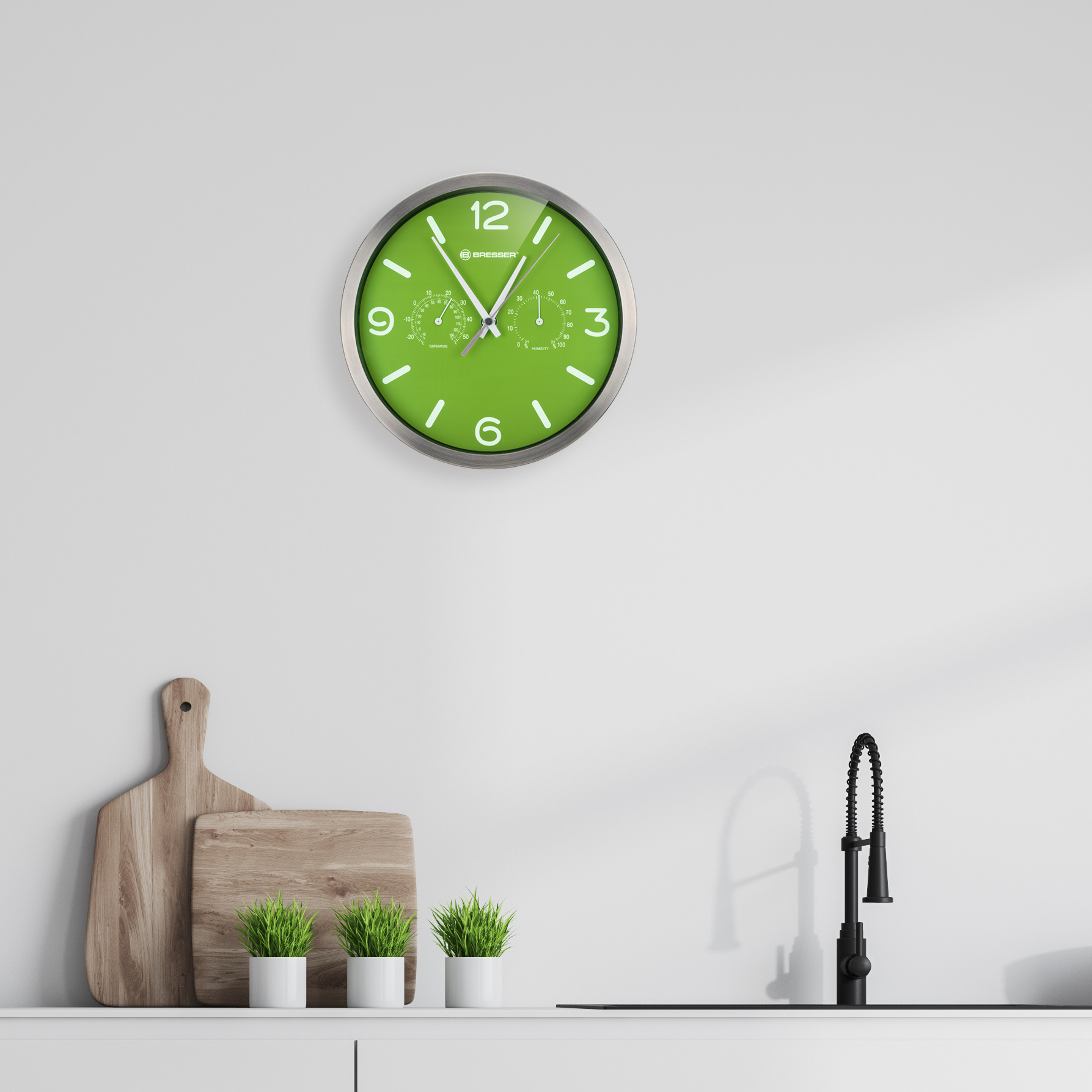 Grüne Uhr mit silbernem Rahmen, an einer weißen Wand.