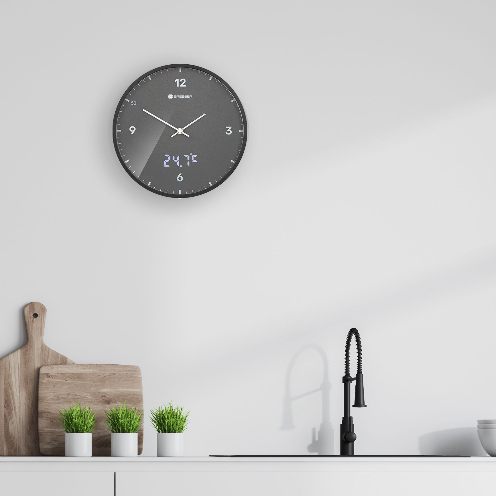Reloj negro con pantalla digital que muestra la hora y la temperatura en una pared blanca sobre un fregadero.