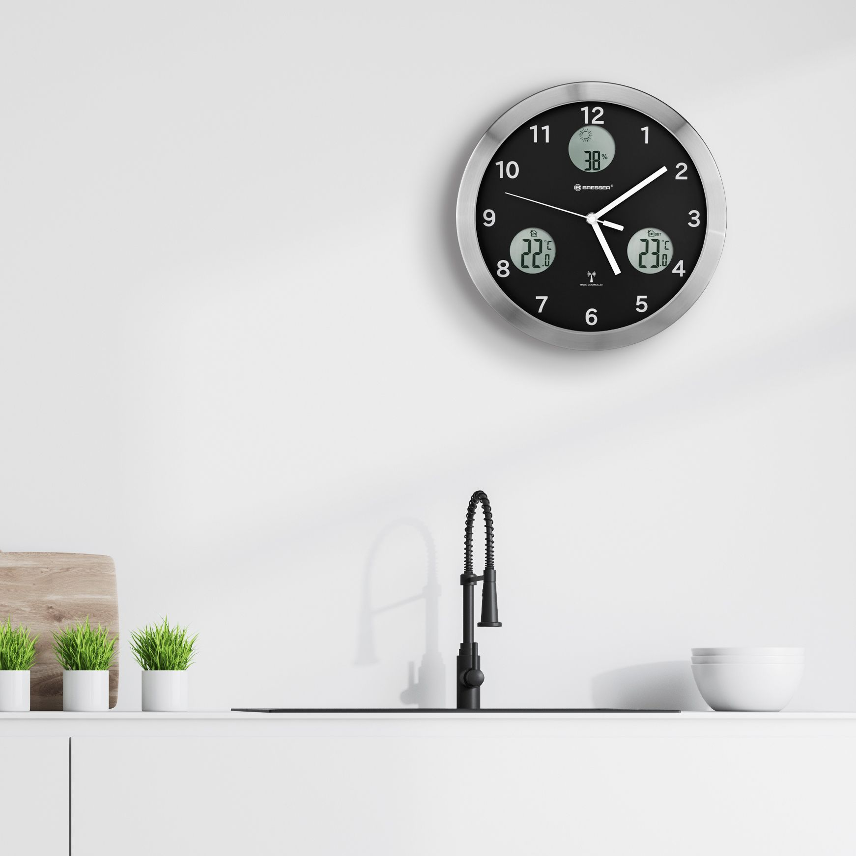 Reloj negro y plateado en una pared blanca sobre un fregadero.