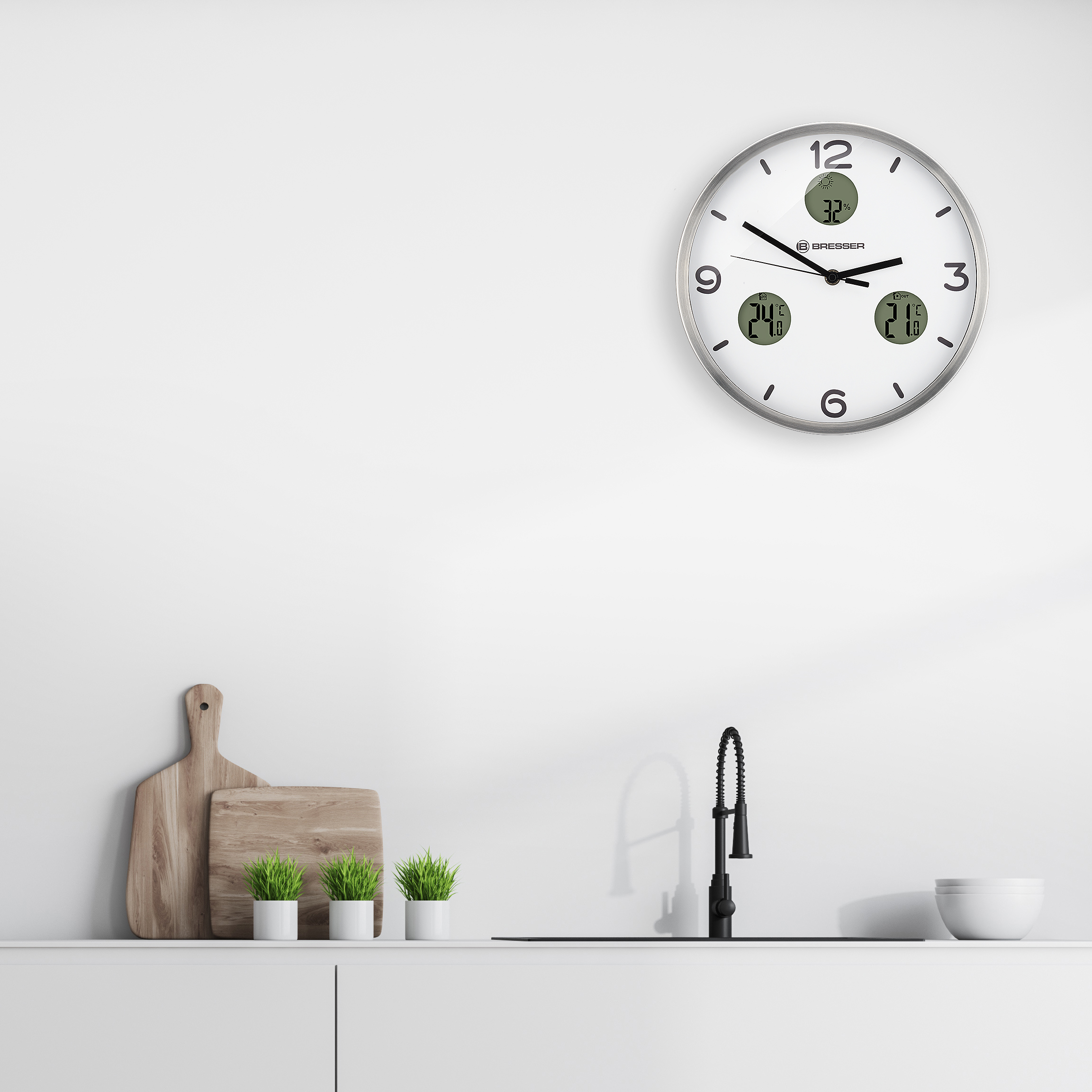 Encimera de cocina blanca con reloj, fregadero y plantas, contra pared blanca.