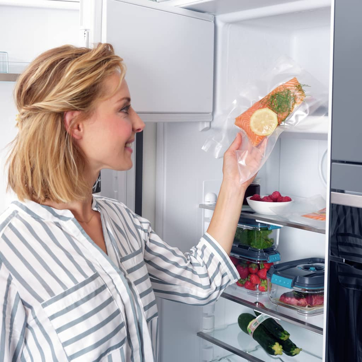 Donna che tiene un filetto di salmone sottovuoto in frigo con altro cibo.