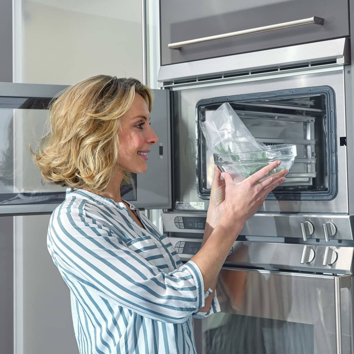 Una donna che mette una ciotola di vetro con cibo in un forno a microonde.