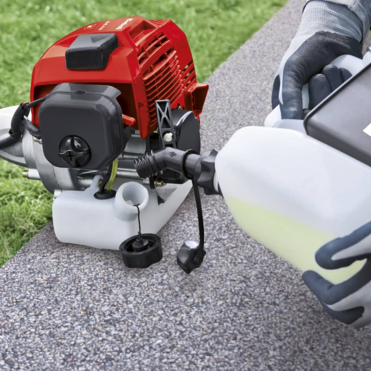 Una persona con guantes está reabasteciendo una máquina roja y gris con un recipiente de combustible blanco.