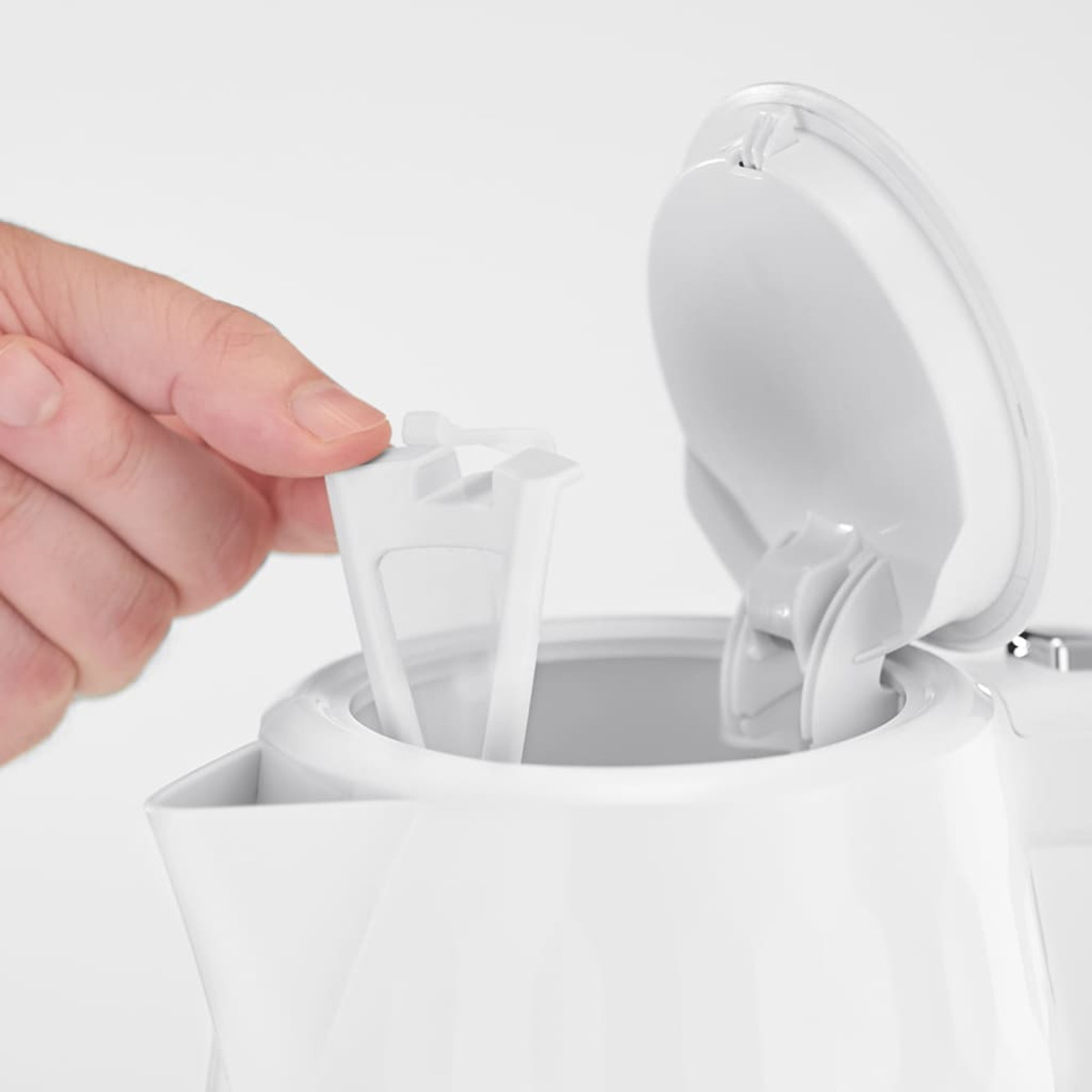Una mano che inserisce un filtro bianco in un bollitore elettrico bianco con il coperchio aperto.