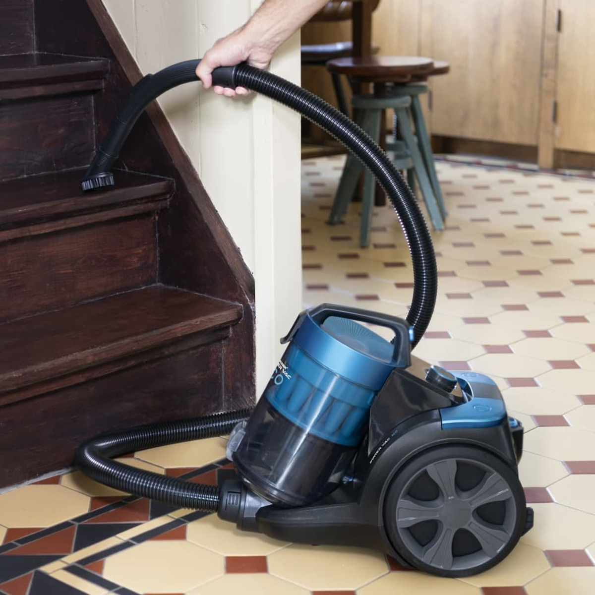 Odkurzacz używany na schodach. Odkurzacz jest czarny i niebieski. Ręka trzyma wąż.
