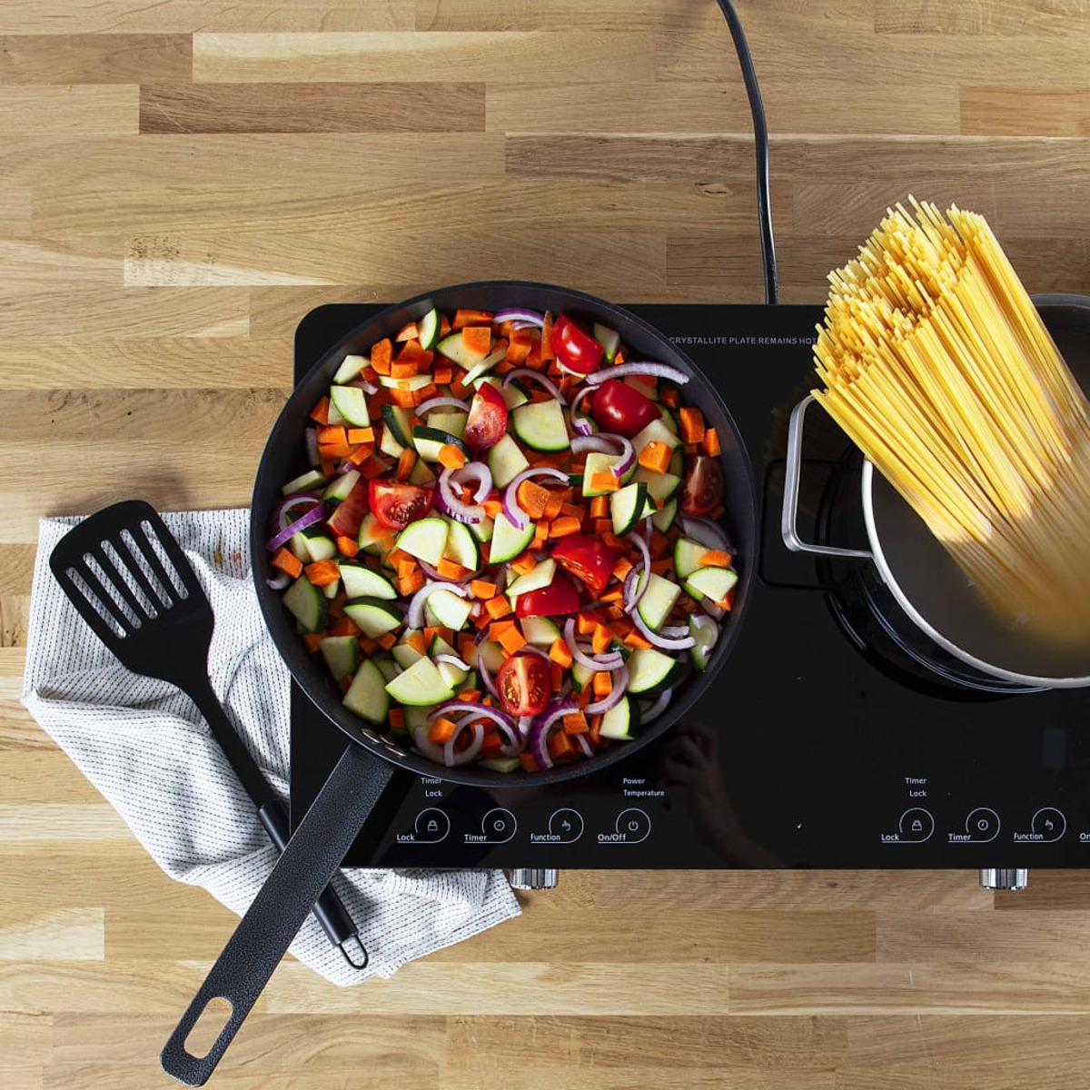 Draufsicht auf Pfanne mit Gemüse, Spaghetti und Kochfläche.