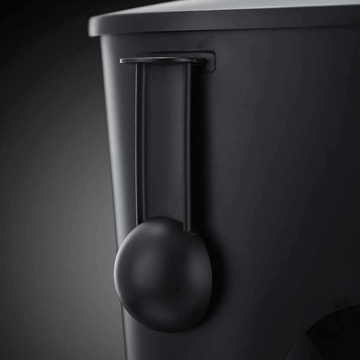 Czarna miarka jest przymocowana do czarnego pojemnika. Miarka jest okrągła, a pojemnik ciemny.