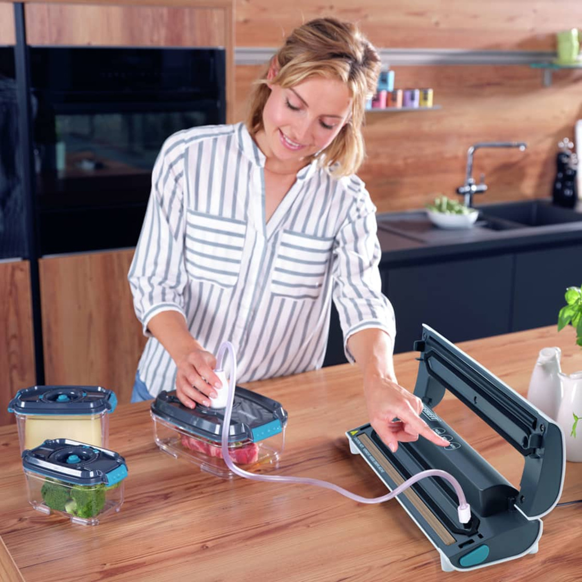 Frau benutzt ein Vakuumiergerät. Drei Behälter mit Lebensmitteln, Maschine auf dem Tisch.
