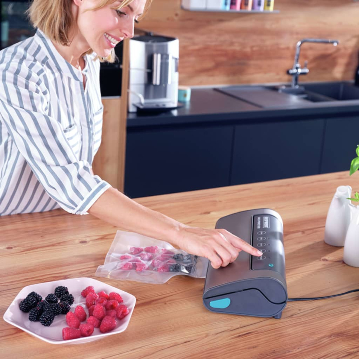Kobieta używa zgrzewarki próżniowej w kuchni. Owoce i worki zgrzewane próżniowo na drewnianym stole.