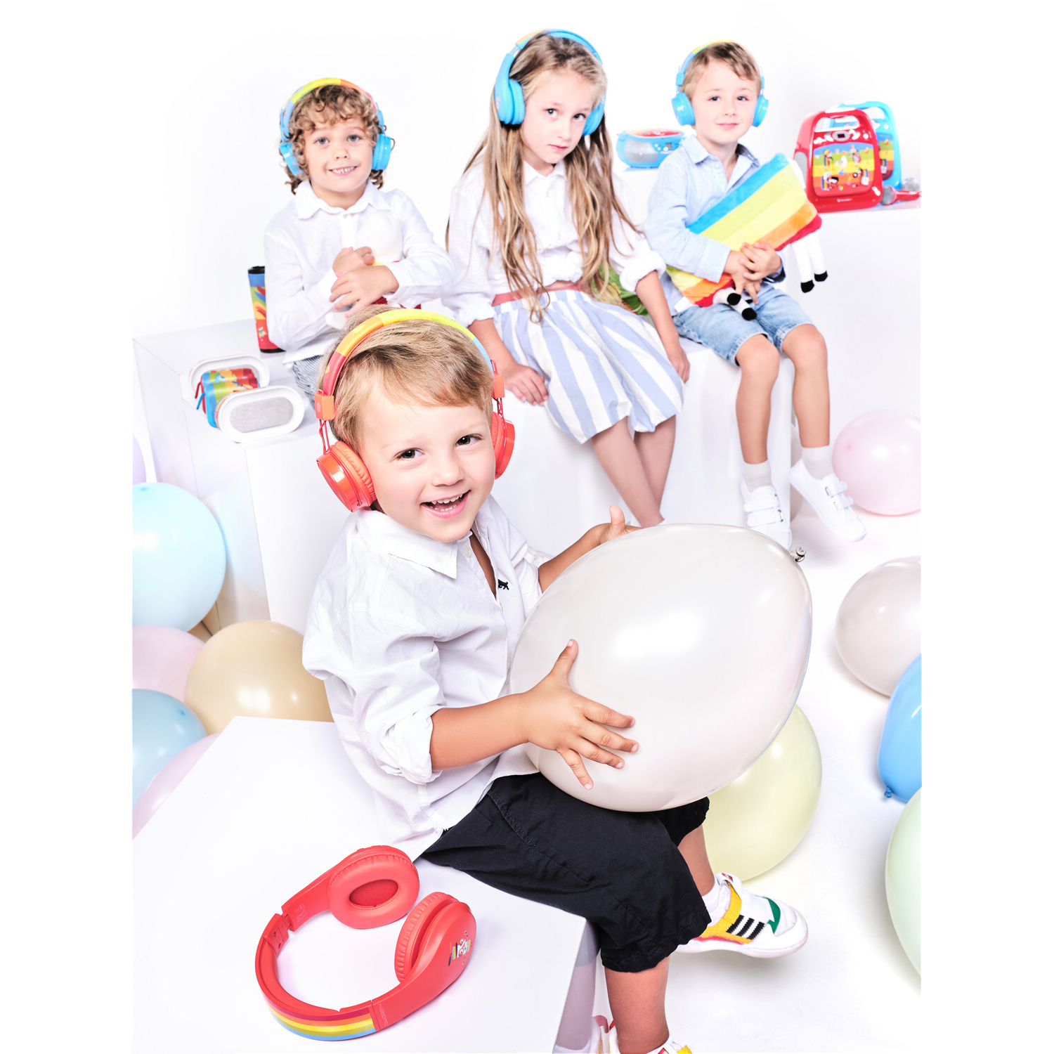 Vier Kinder mit Kopfhörern, lächelnd, halten Spielzeug und Luftballons.