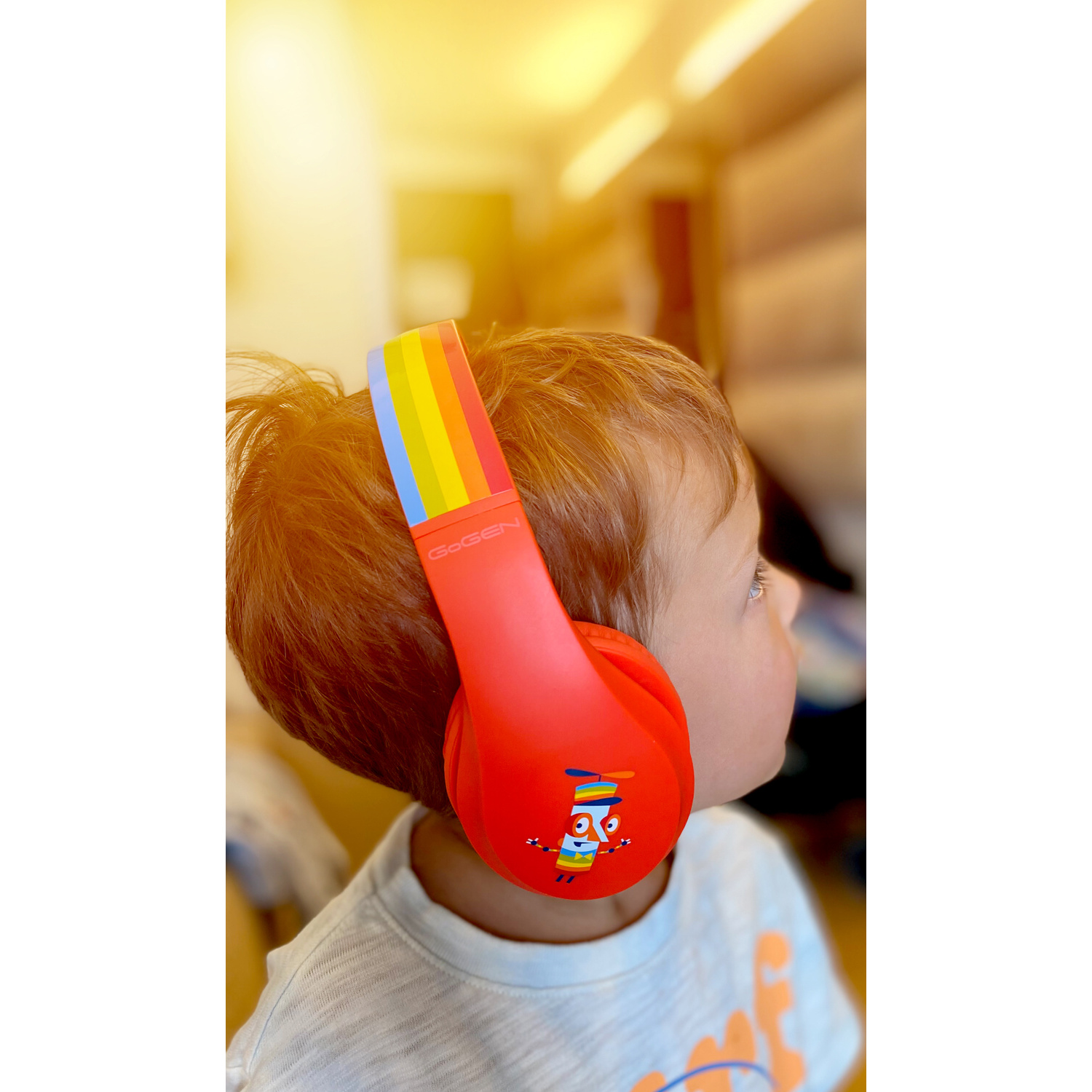 Ein Kind trägt rote Kopfhörer mit Regenbogenmuster auf dem Kopfband. Das Gesicht des Kindes ist sichtbar.