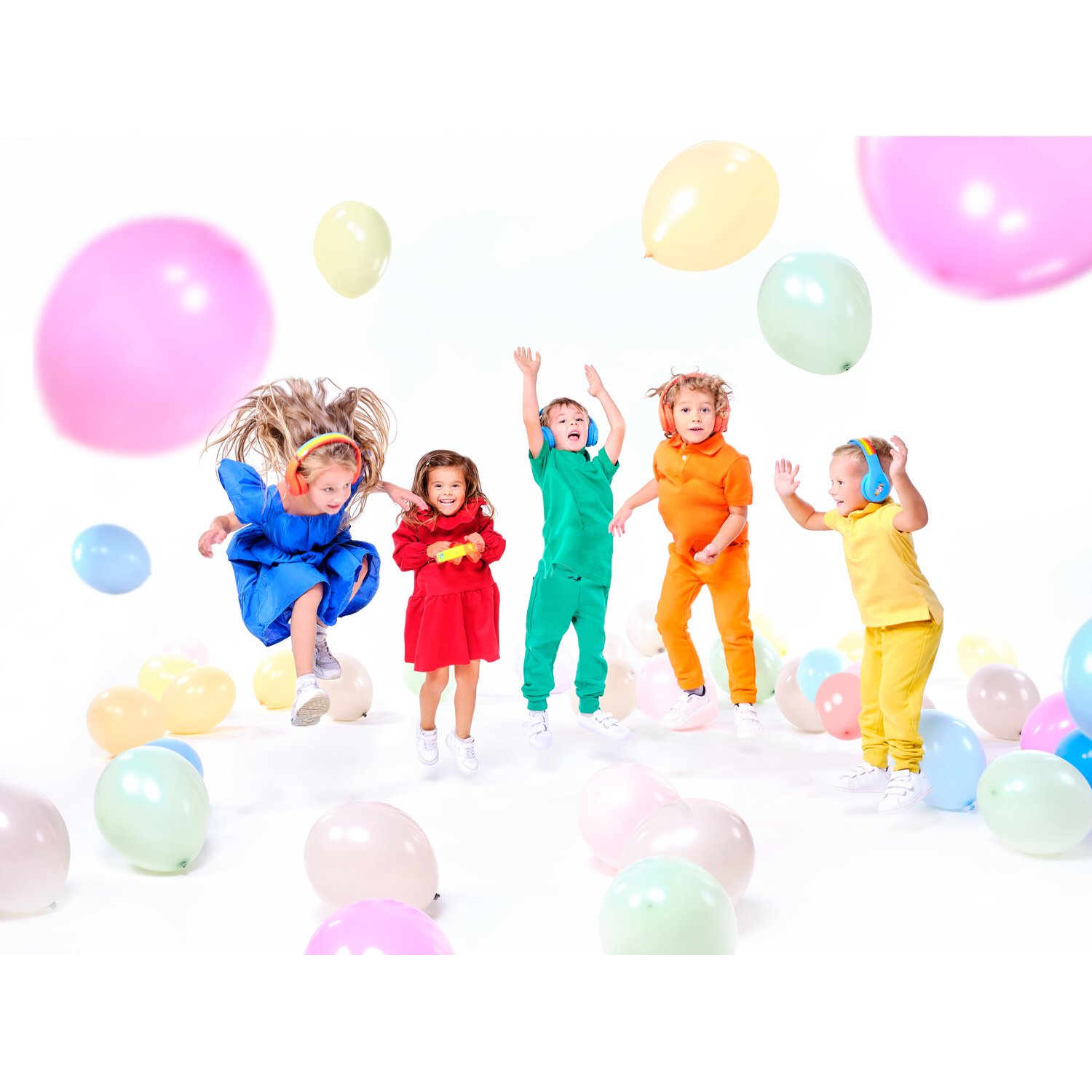 Fünf Kinder springen mit Luftballons. Sie tragen Kopfhörer und bunte Kleidung, weißer Hintergrund.