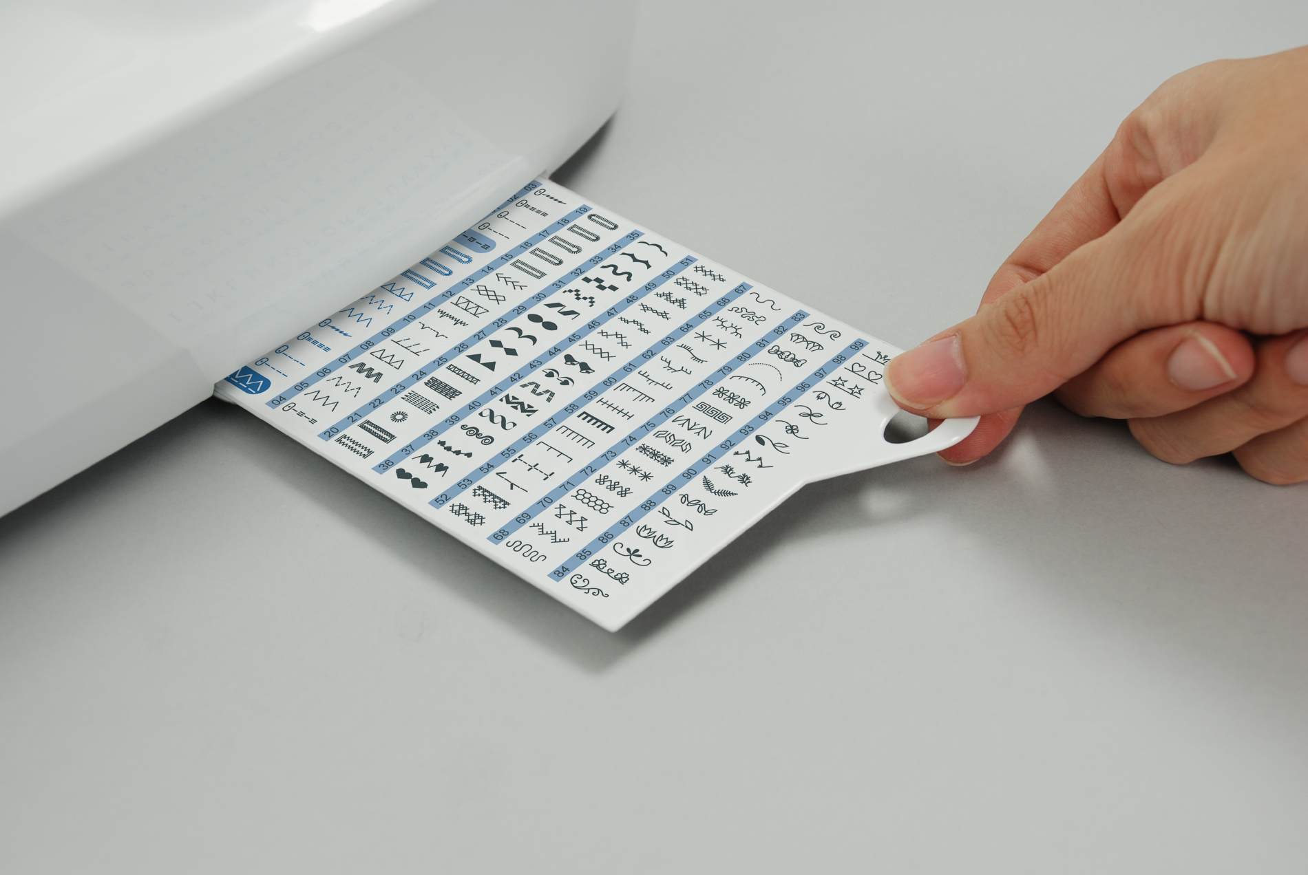 Una mano sacando una tabla de puntadas de una máquina de coser blanca. La tabla es azul claro.
