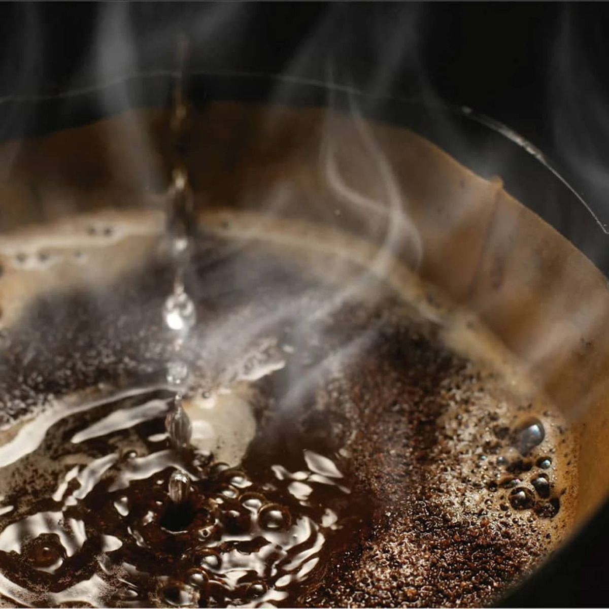 Primo piano della preparazione del caffè con vapore che sale. L'acqua gocciola attraverso il caffè macinato in un filtro.