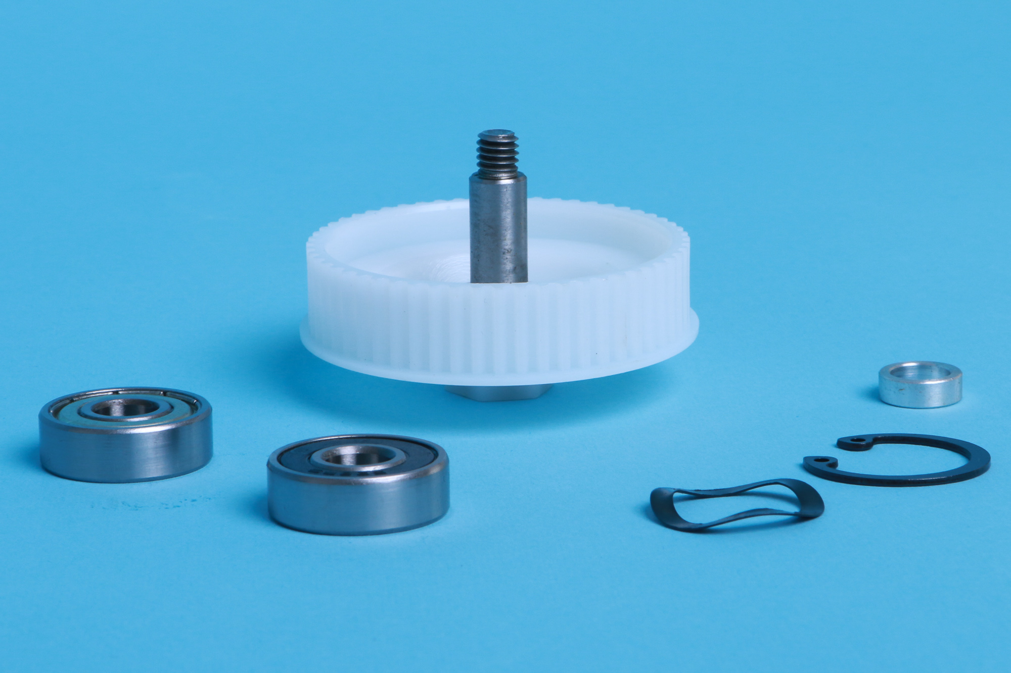 Verschiedene mechanische Teile: Zahnrad, Lager und Sicherungsring auf blauem Hintergrund.