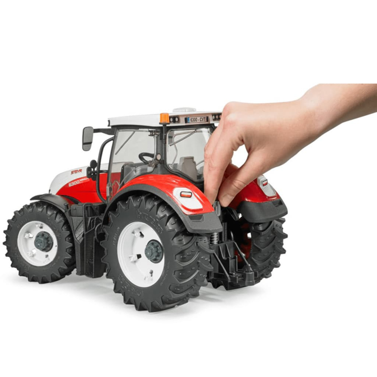 Czerwony i biały traktor zabawka, ręka dotyka tyłu. Białe tło.