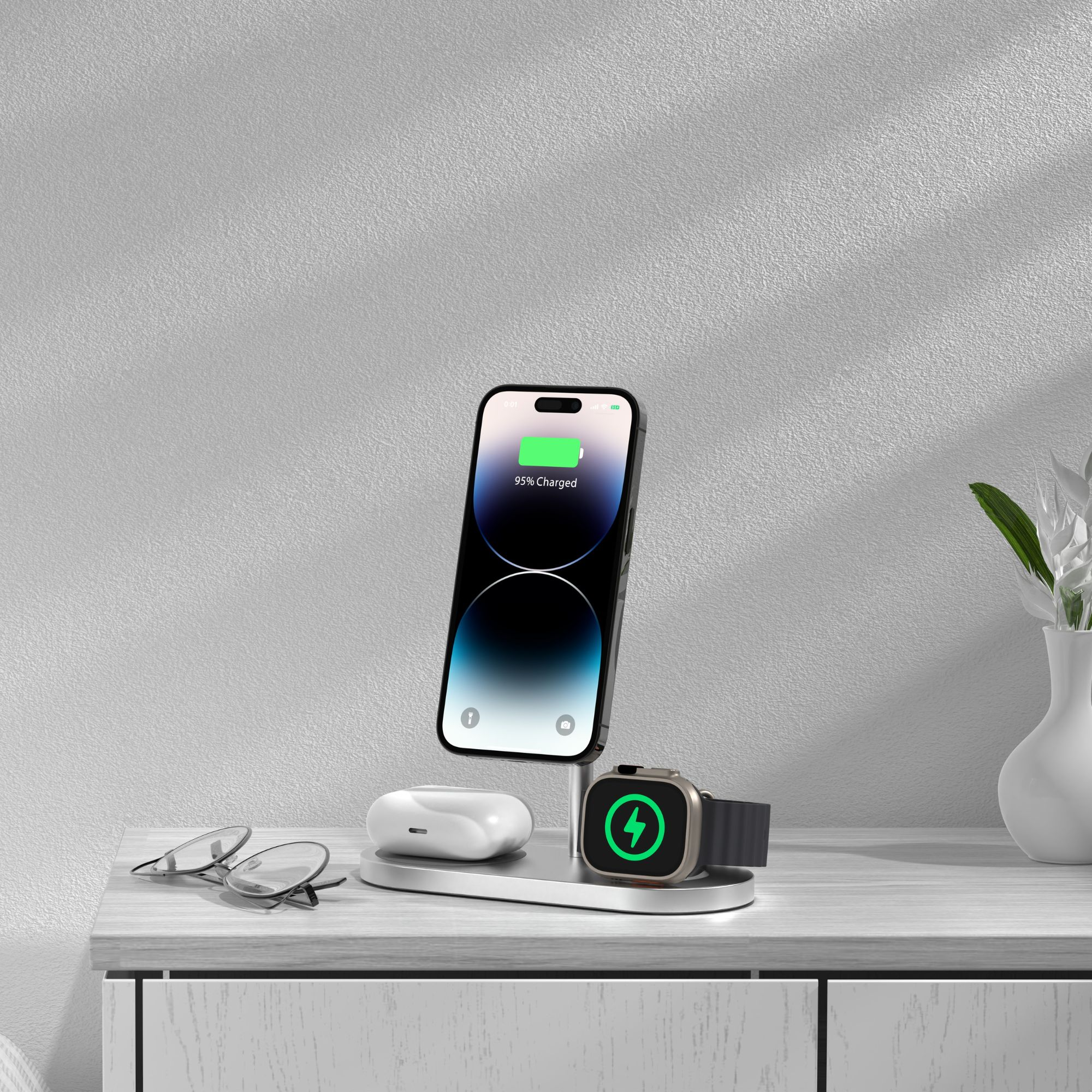 Stazione di ricarica con telefono, orologio e auricolari. Il telefono mostra il 95% di carica. Occhiali sul tavolo.