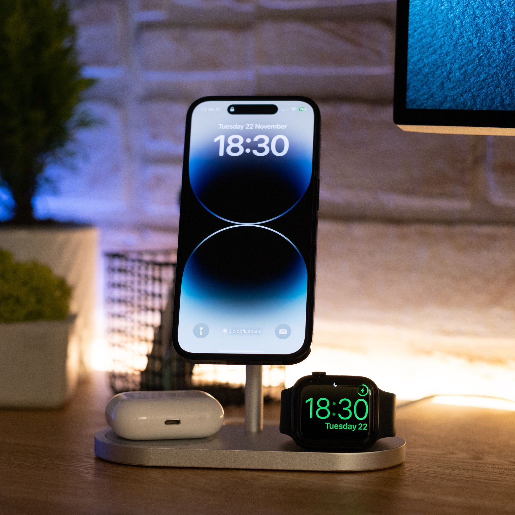 Telefono, orologio e auricolari su un supporto di ricarica. Il telefono mostra l'ora. Sfondo scuro.