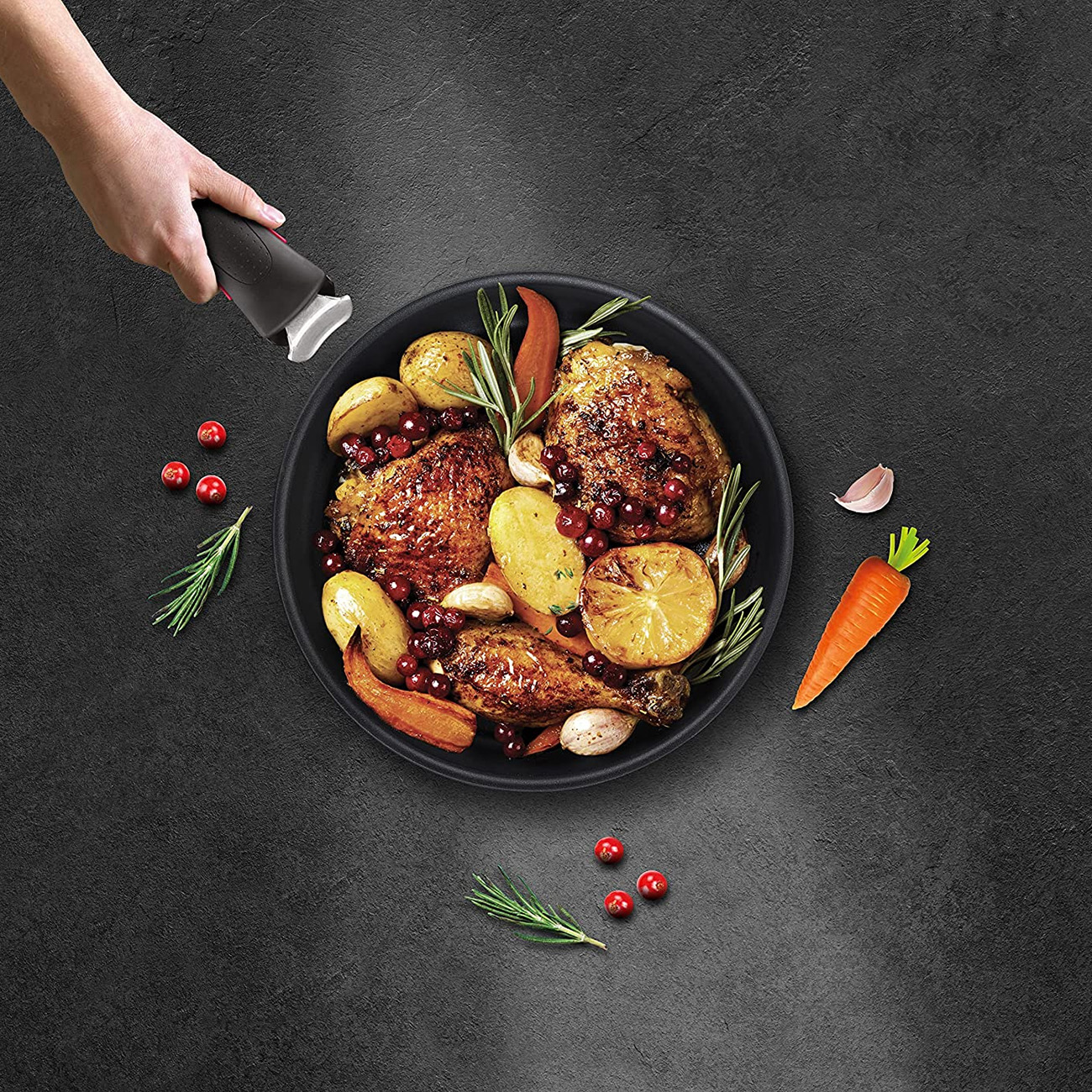 Vista aérea de pollo, patatas y verduras en una sartén con una mano sujetando el mango.