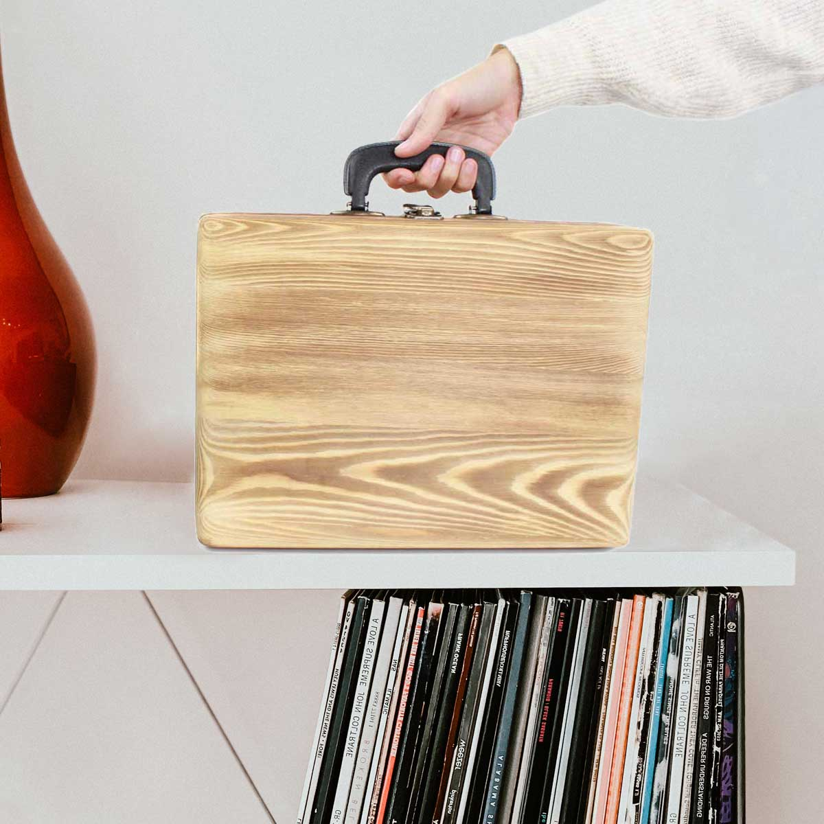 Dłoń osoby trzymającej drewnianą skrzynkę na półce. Poniżej półki znajdują się płyty.