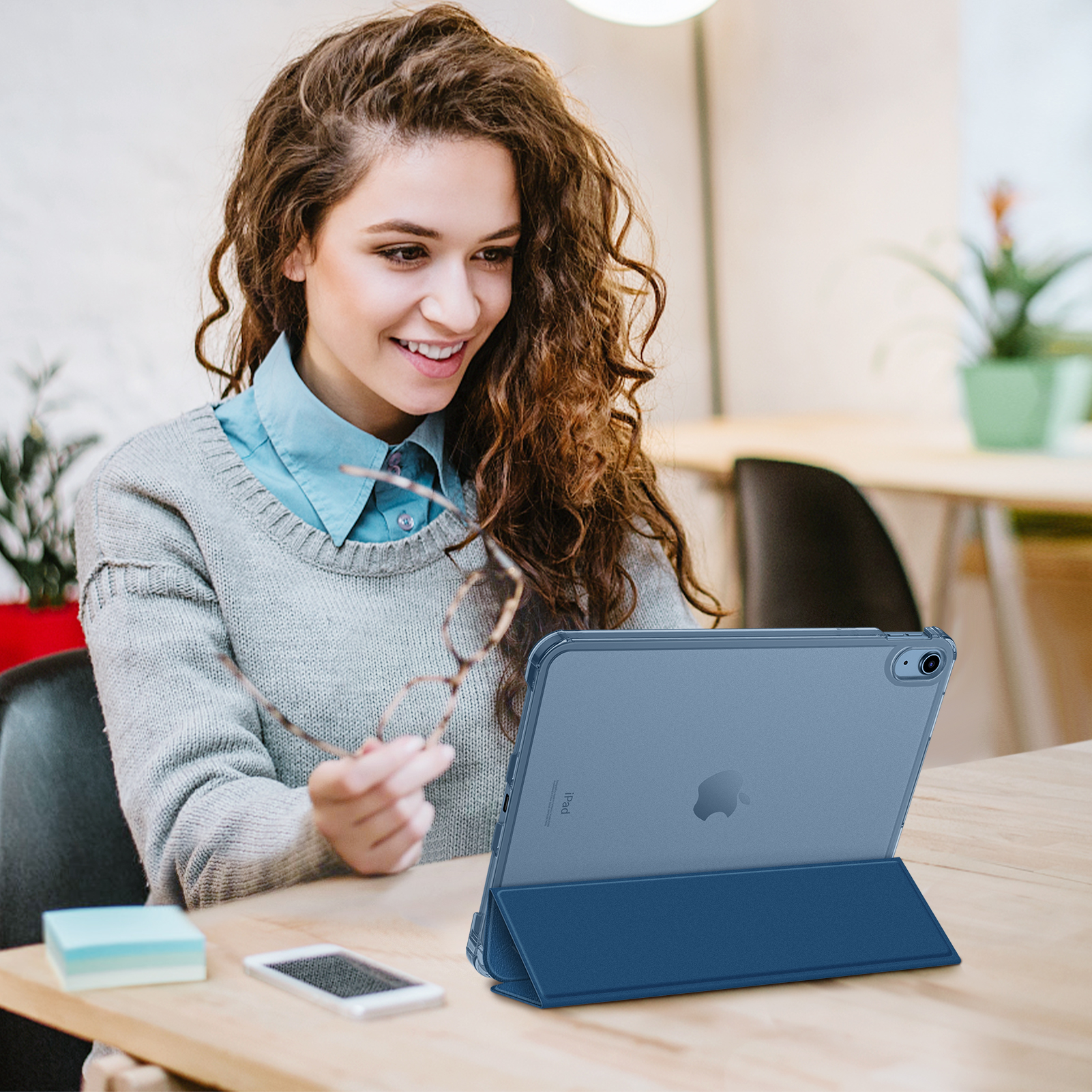 Frau mit Brille betrachtet Tablet, Tisch, Handy.
